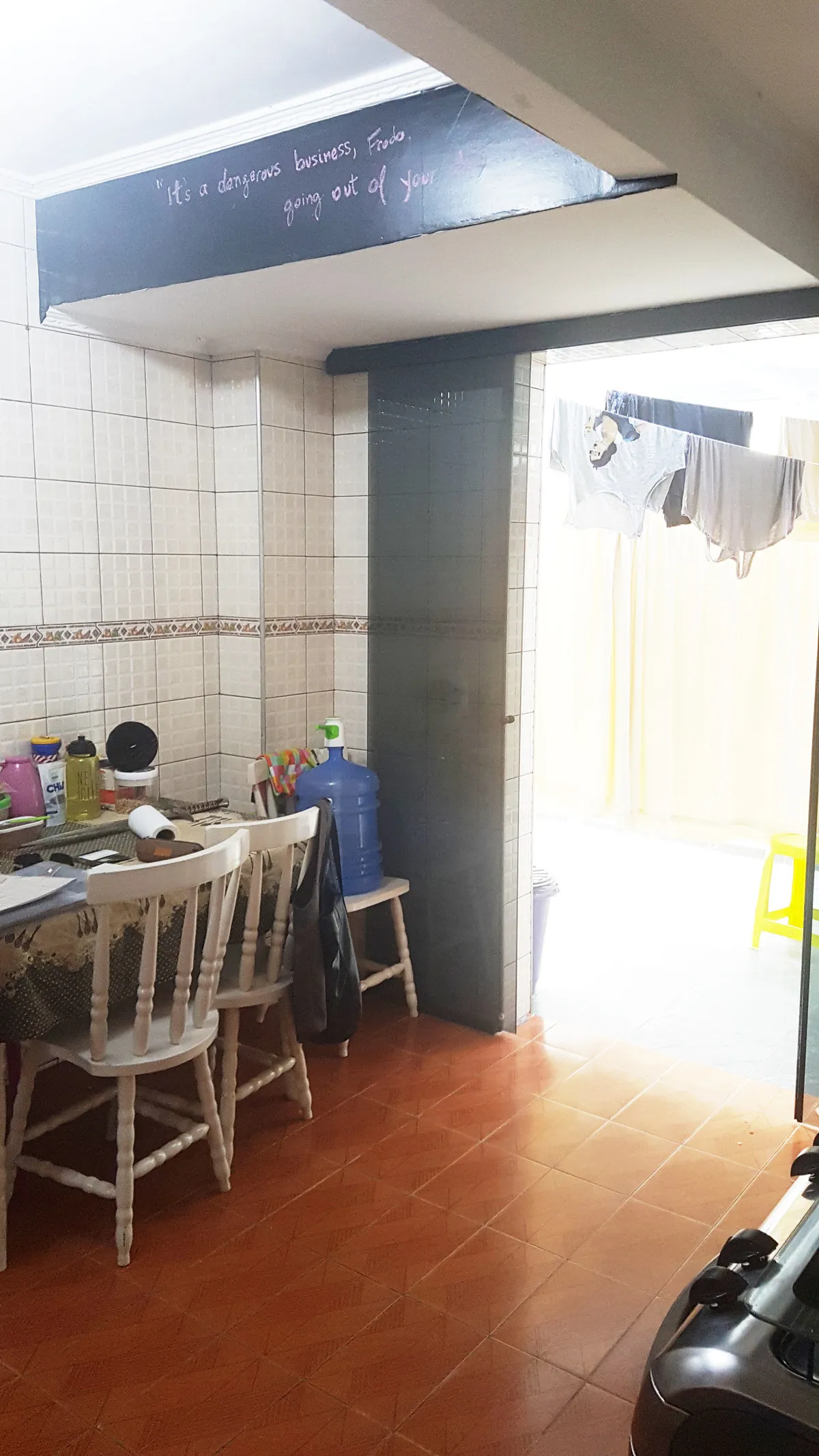 Cozinha antiga com azulejo branco, viga pintada de azul, piso vermelho e mesa junto à área de serviço, antes da reforma
