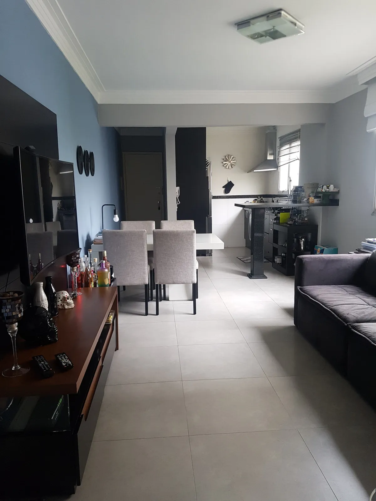 Sala, jantar e cozinha integrados com parede azul, TV, buffet de madeira escura e mesa branca, antes da reforma