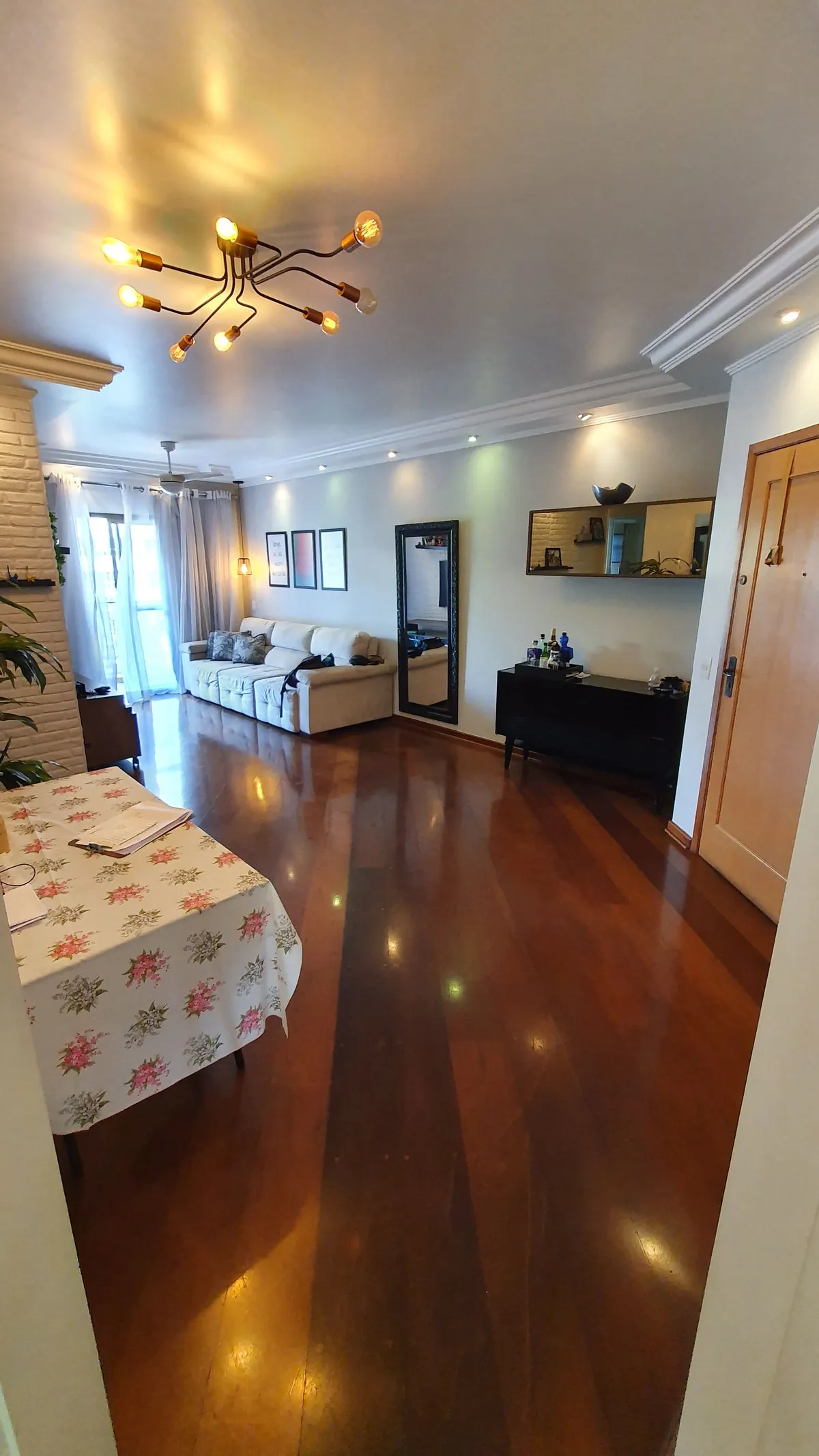 Sala ampla com piso de madeira escura envernizada, sofá bege, espelho de chão e forro de gesso, antes da reforma