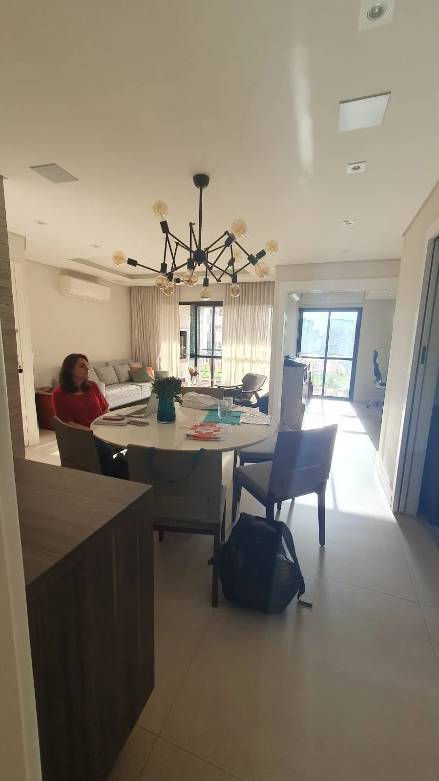 Sala de estar e jantar antigas com mesa redonda branca, lustre de filamento e sofá cinza, antes da reforma