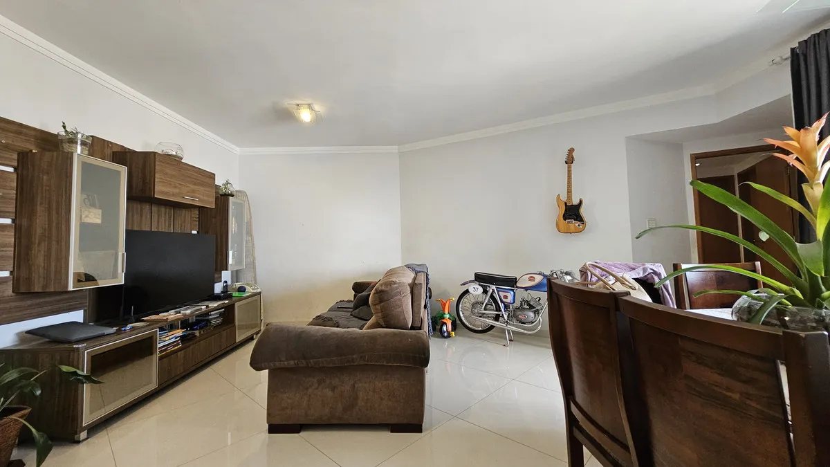 Sala com estante de madeira escura, TV, sofás marrom de tecido e moto antiga exposta, antes da reforma