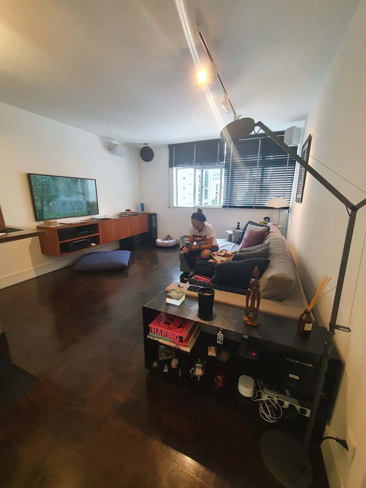 Sala ampla com buffet ripado de madeira, sofá cinza e piso de taco escuro, antes da reforma