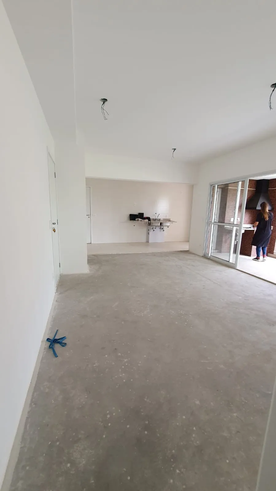 Sala ampla vazia com contrapiso de cimento, paredes brancas e fiação solta no teto, antes da reforma