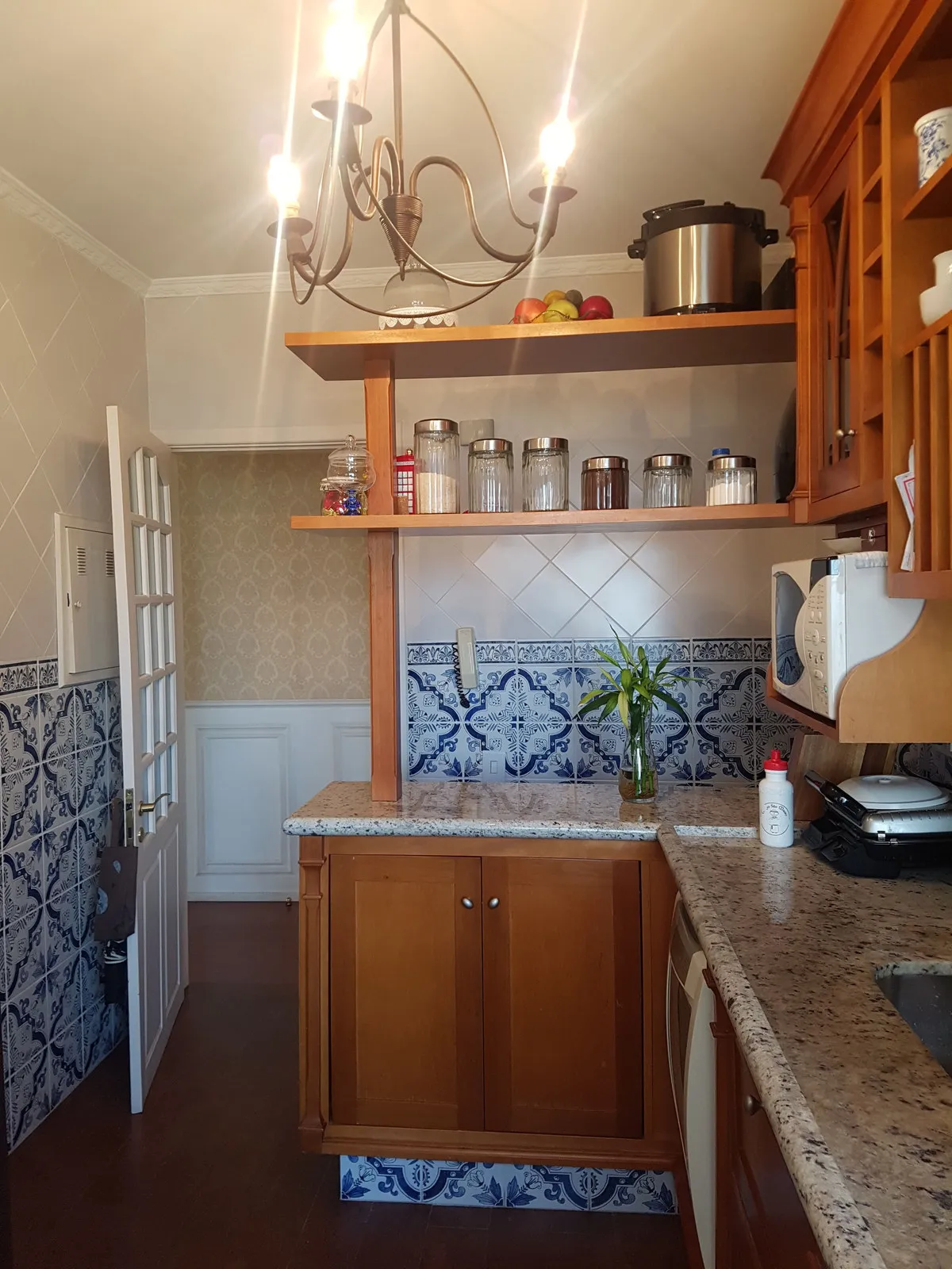 Cozinha estreita com armários de madeira envernizada, azulejo português azul e branco e bancada de granito, antes da reforma