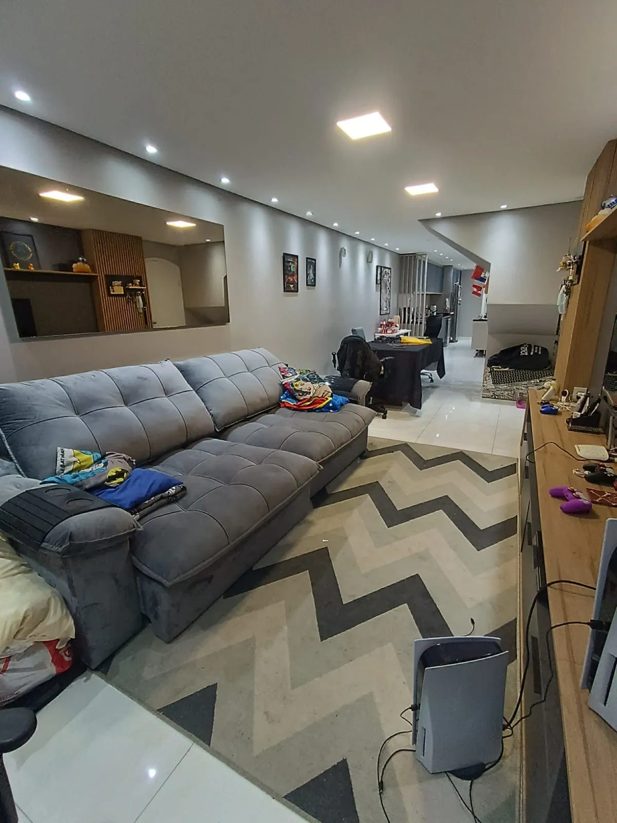 Sala de estar com sofá cinza, tapete de zigue-zague e painel de madeira para TV, antes da reforma