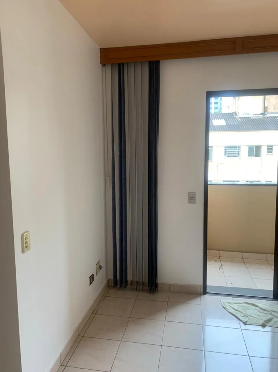 Cômodo vazio com porta de correr para a varanda, persiana vertical e piso de cerâmica bege, antes da reforma