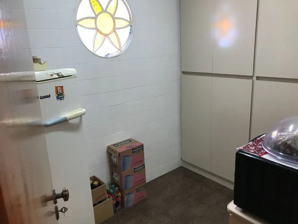 Copa com azulejo branco, geladeira, janela redonda de vitral e caixas no chão, antes da reforma