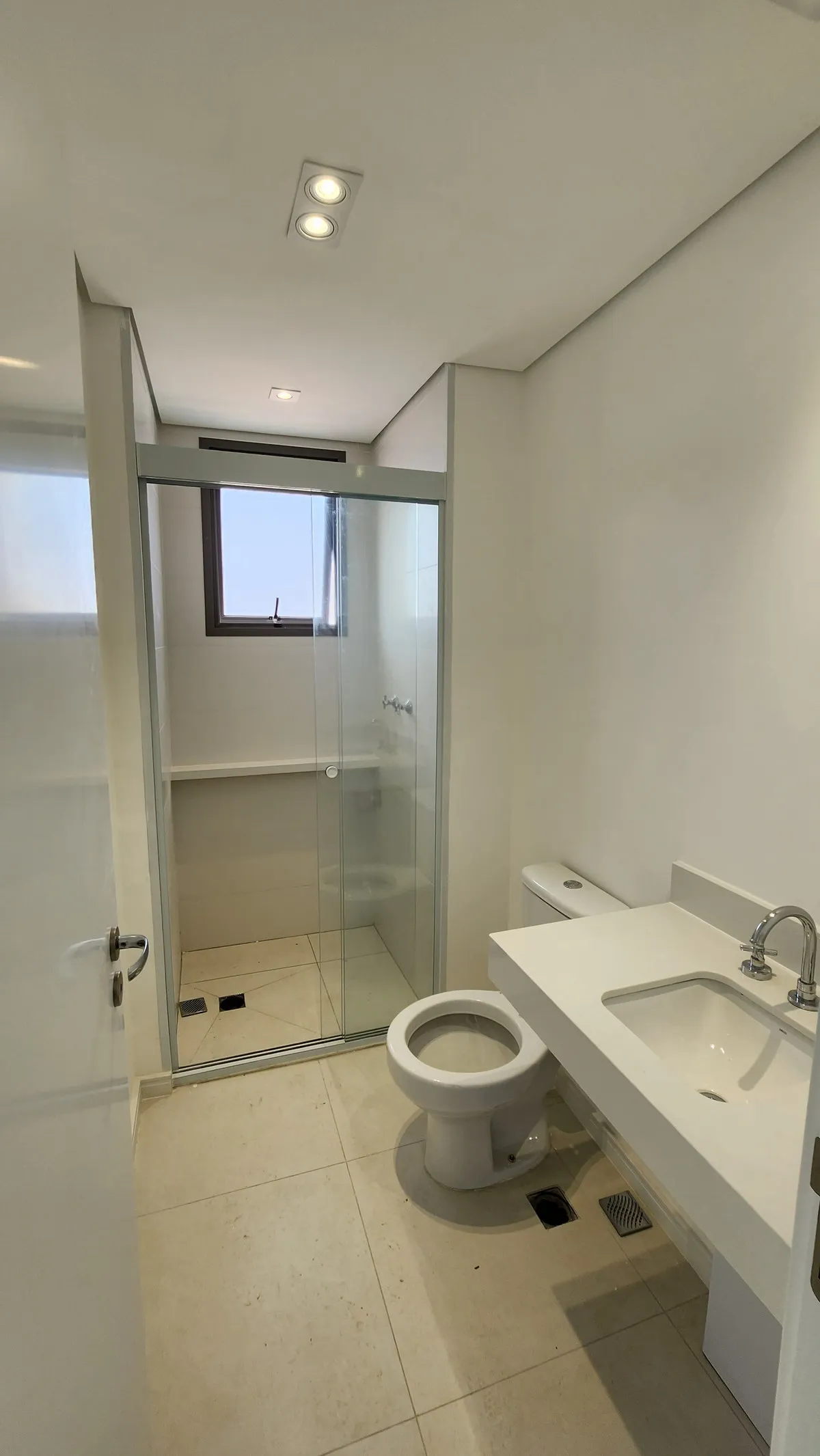 Banheiro com box de vidro, vaso sanitário e bancada branca com cuba, antes da reforma
