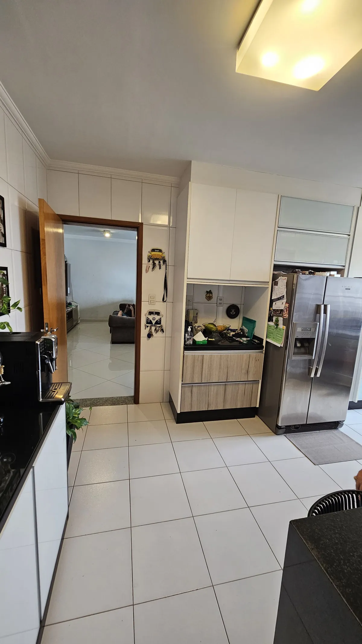 Cozinha com piso de porcelanato branco, armários brancos, geladeira inox e luminária amarelada, antes da reforma