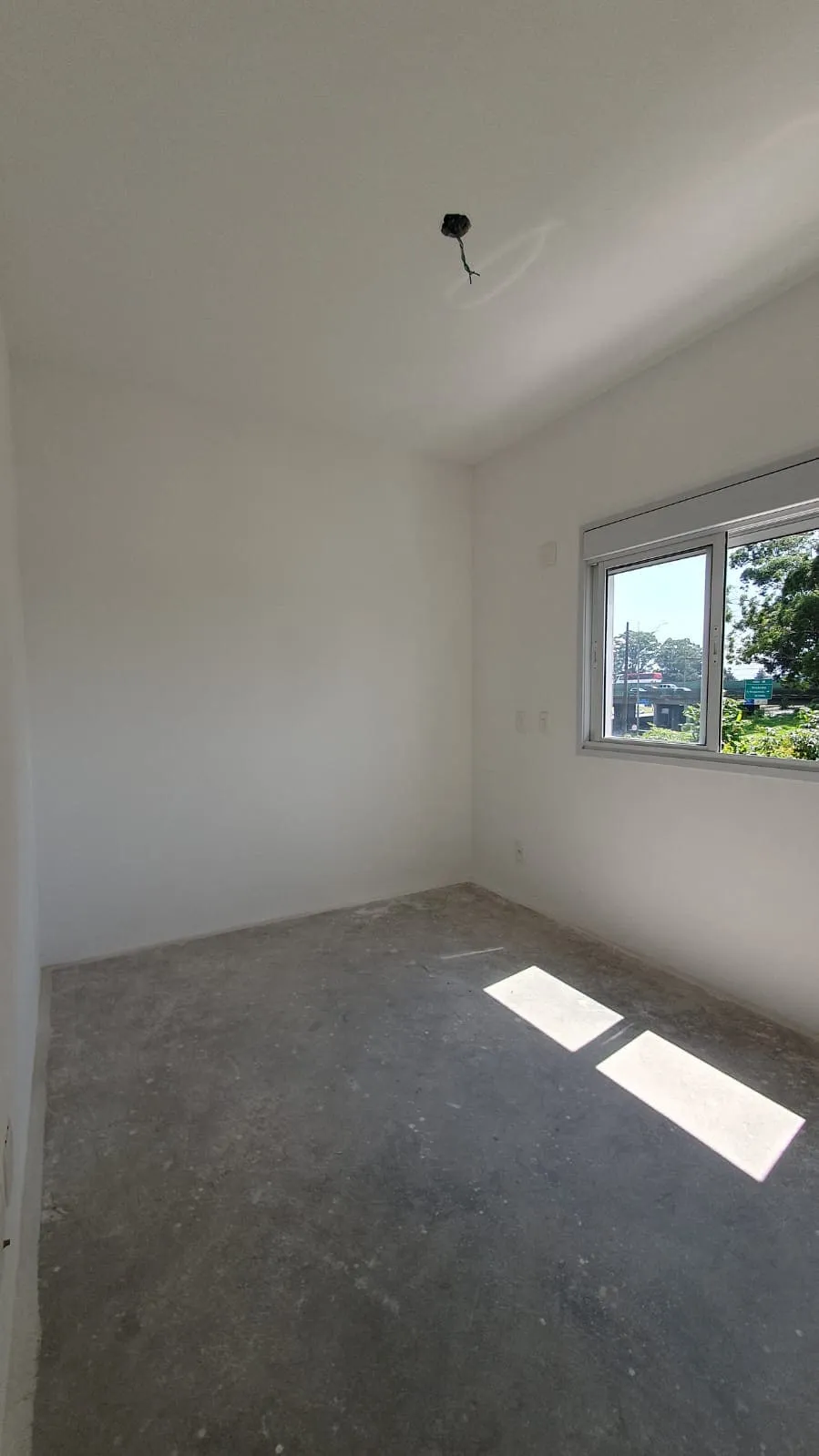Quarto vazio com contrapiso de cimento, janela de correr com vista para a rua e ponto de luz solto, antes da reforma
