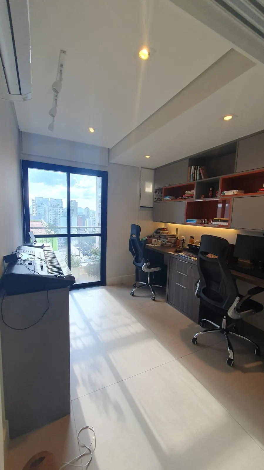 Canto musical antigo com teclado, janela de piso ao teto com vista da cidade e marcenaria cinza, antes da reforma