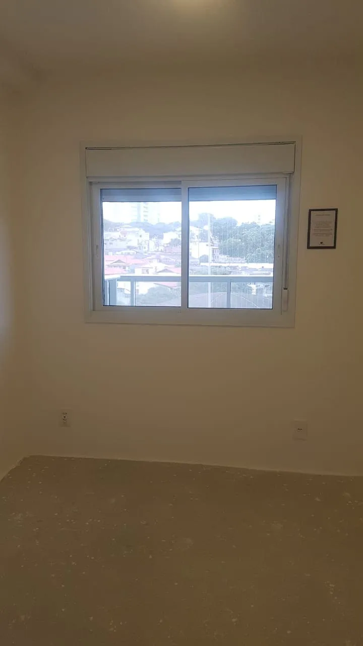 Quarto vazio com janela de correr voltada para a cidade e piso de contrapiso cru, antes da reforma
