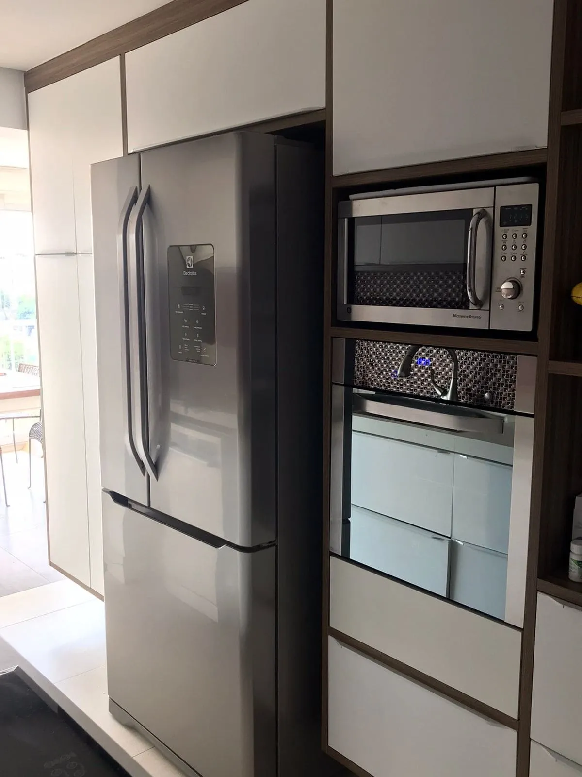 Cozinha com geladeira inox, micro-ondas e forno embutidos na marcenaria branca, antes da reforma