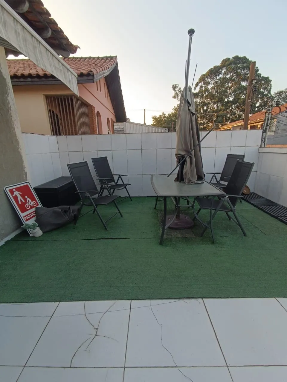 Terraço com grama sintética, mesa de vidro, cadeiras dobráveis e ombrelone fechado, antes da reforma