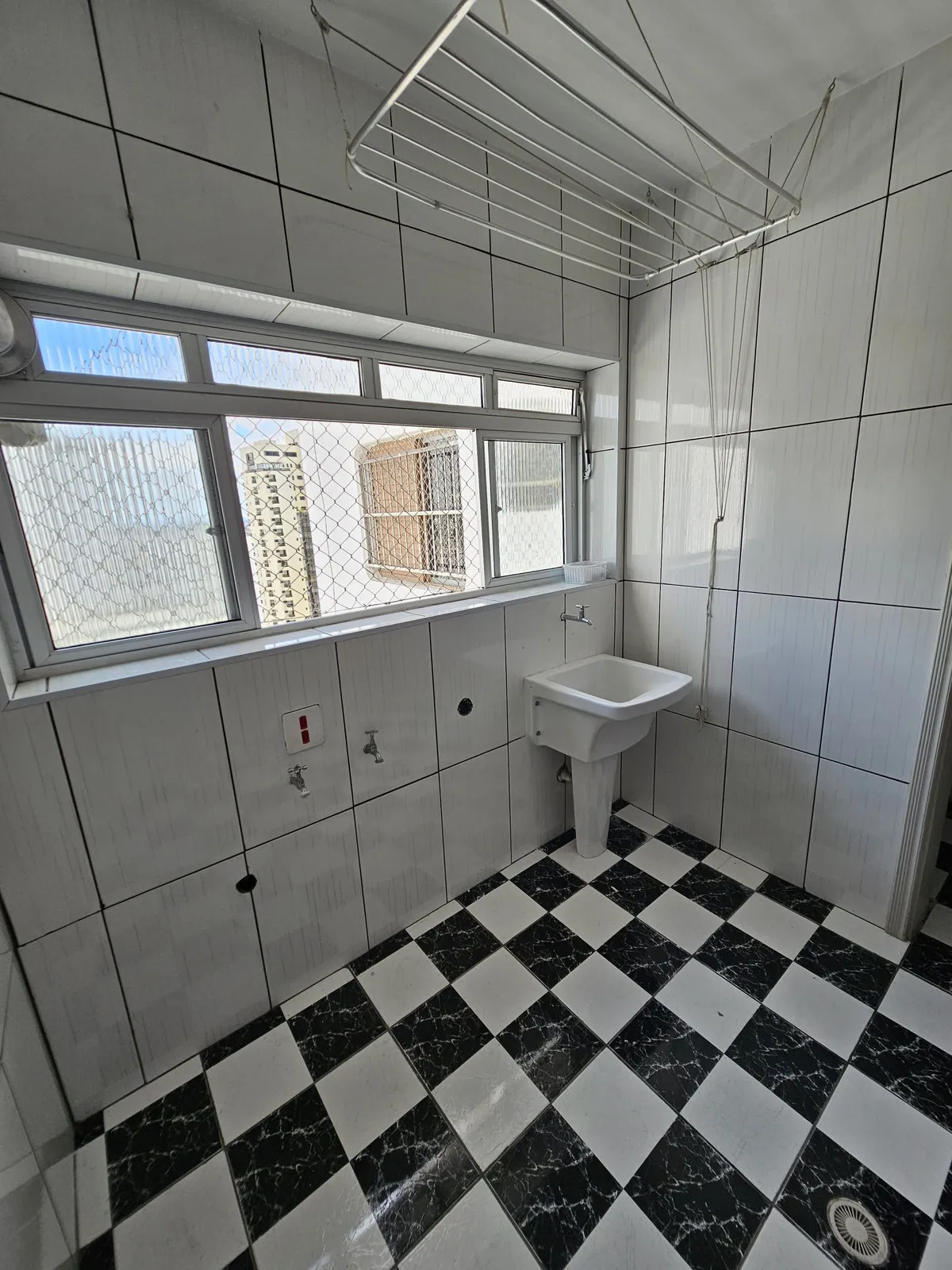 Área de serviço com azulejo branco, tanque de louça, varal suspenso e janela, antes da reforma