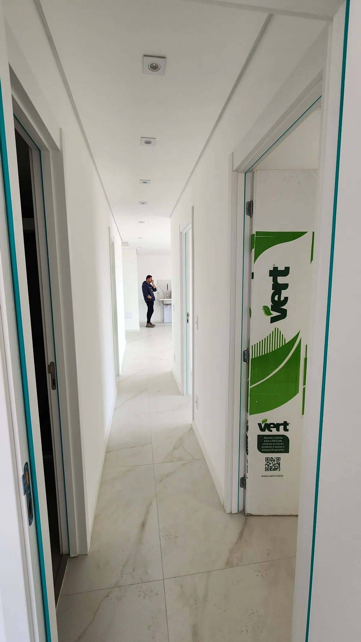 Corredor comprido com piso marmorizado e portas ainda protegidas por película, antes da reforma