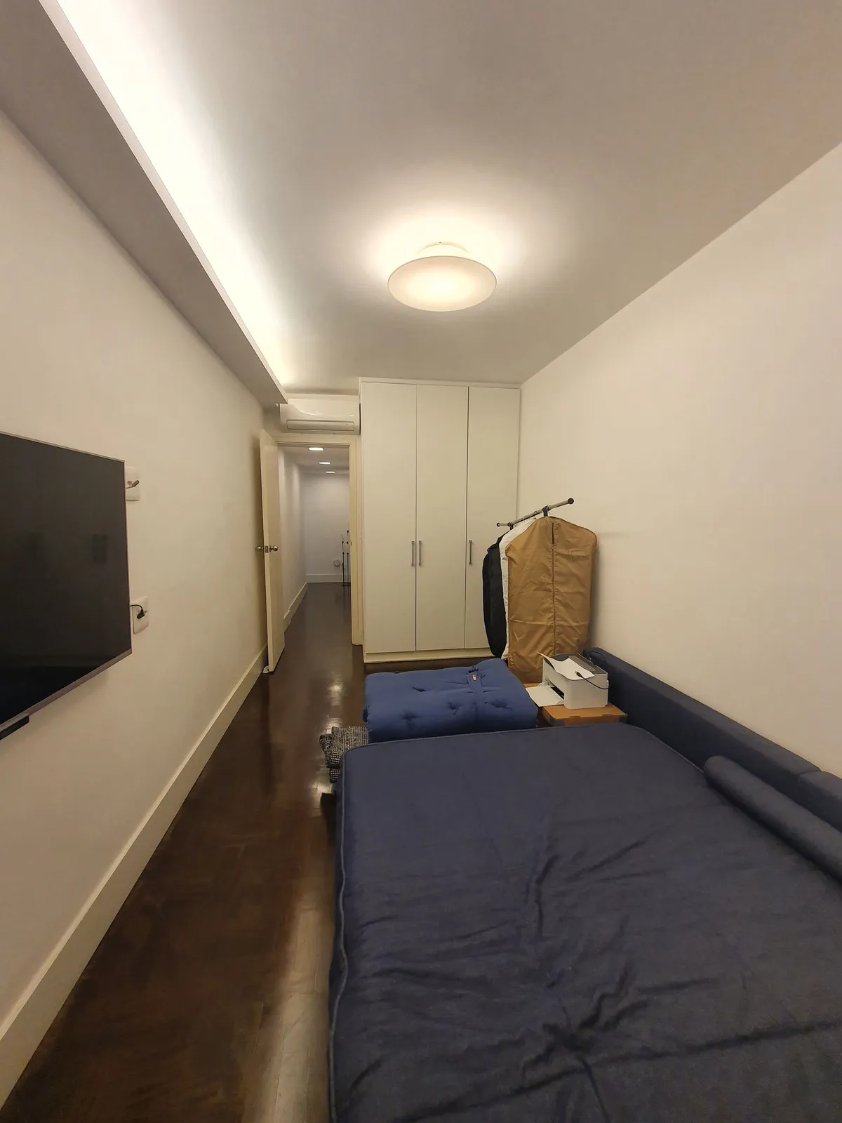 Quarto estreito com guarda-roupa branco, TV na parede e colchão azul no chão, antes da reforma