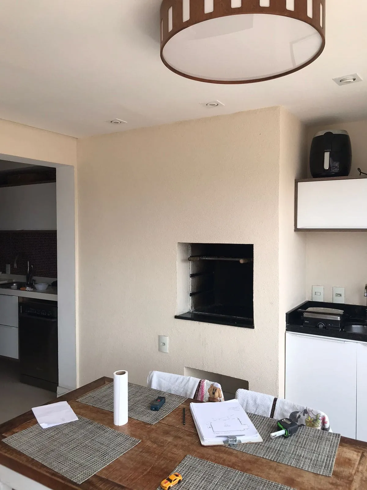 Varanda com churrasqueira embutida na parede clara e cozinha ao fundo, antes da reforma