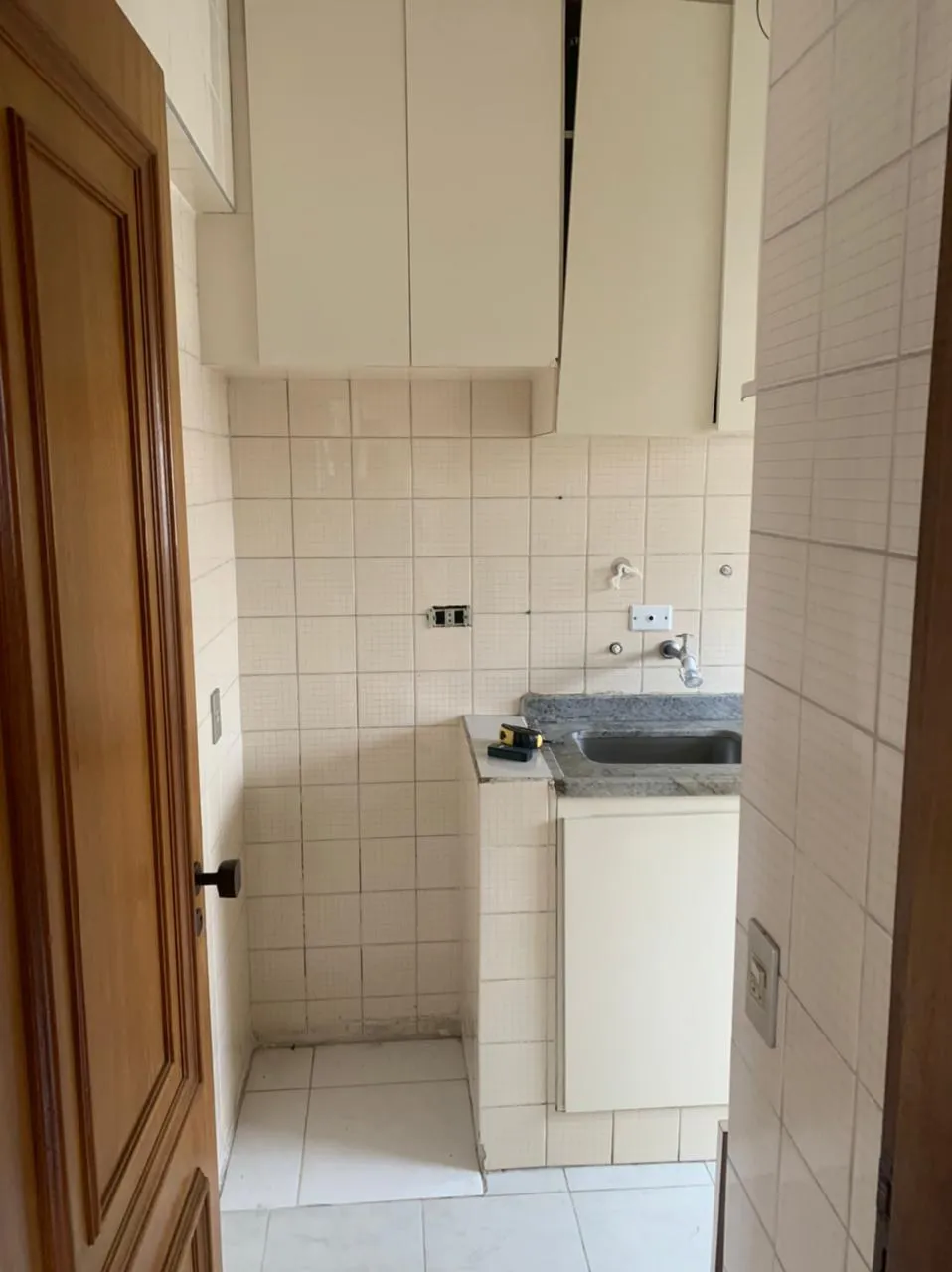 Cozinha compacta com azulejo branco, armários brancos, bancada de granito com cuba e porta de madeira, antes da reforma