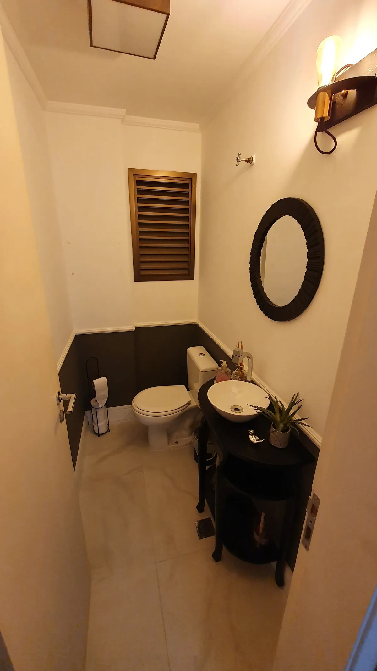 Lavabo com parede bicolor marrom e branca, espelho redondo e bancada preta com cuba, antes da reforma