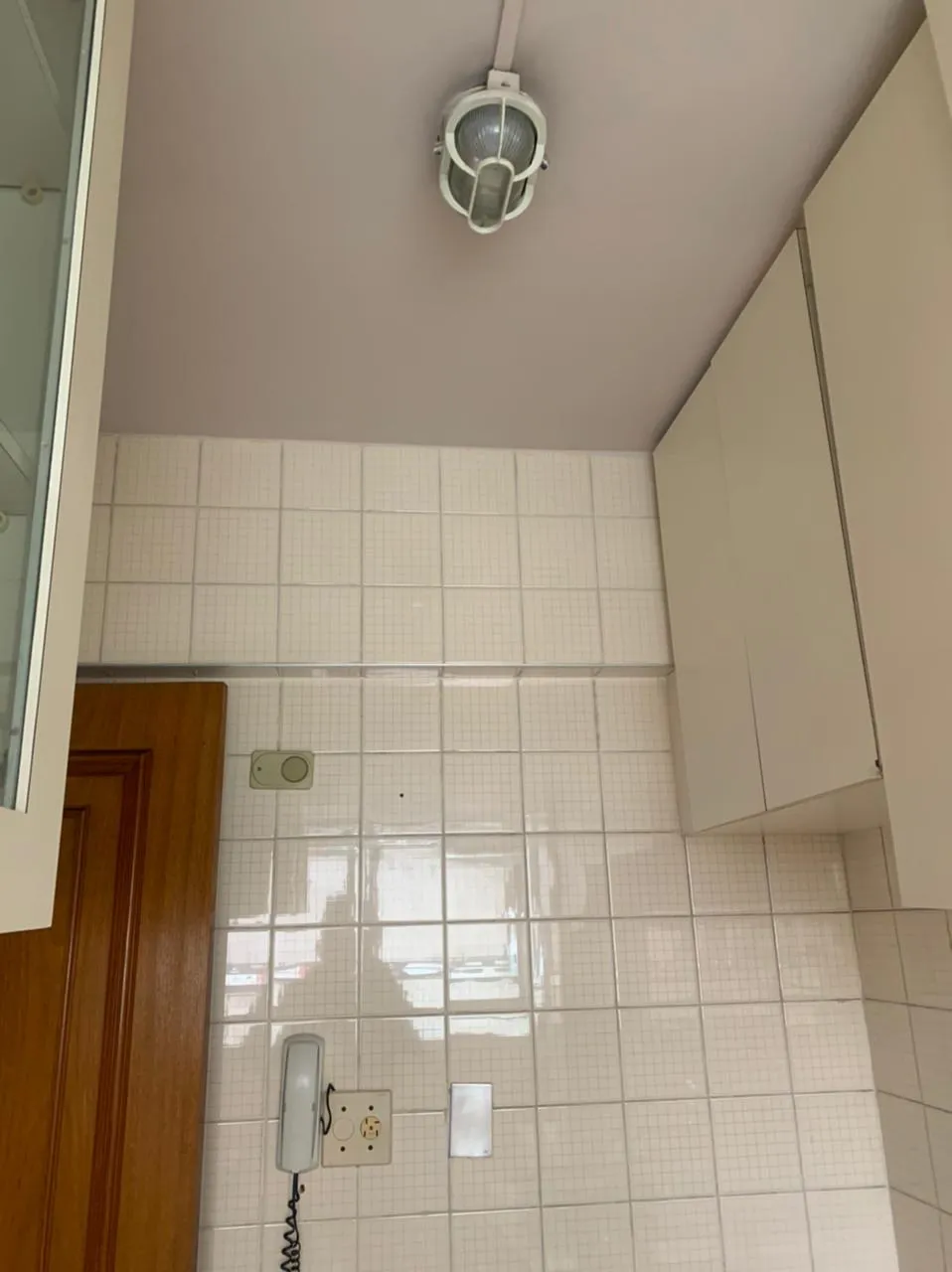 Área de serviço com azulejo branco, luminária tartaruga no teto lilás e interfone, antes da reforma