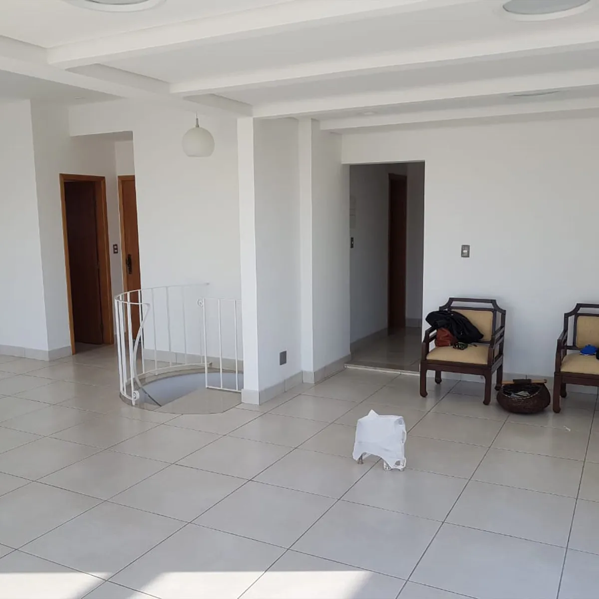 Ambiente vazio com paredes brancas, piso de porcelanato e guarda-corpo de escada caracol, antes da reforma