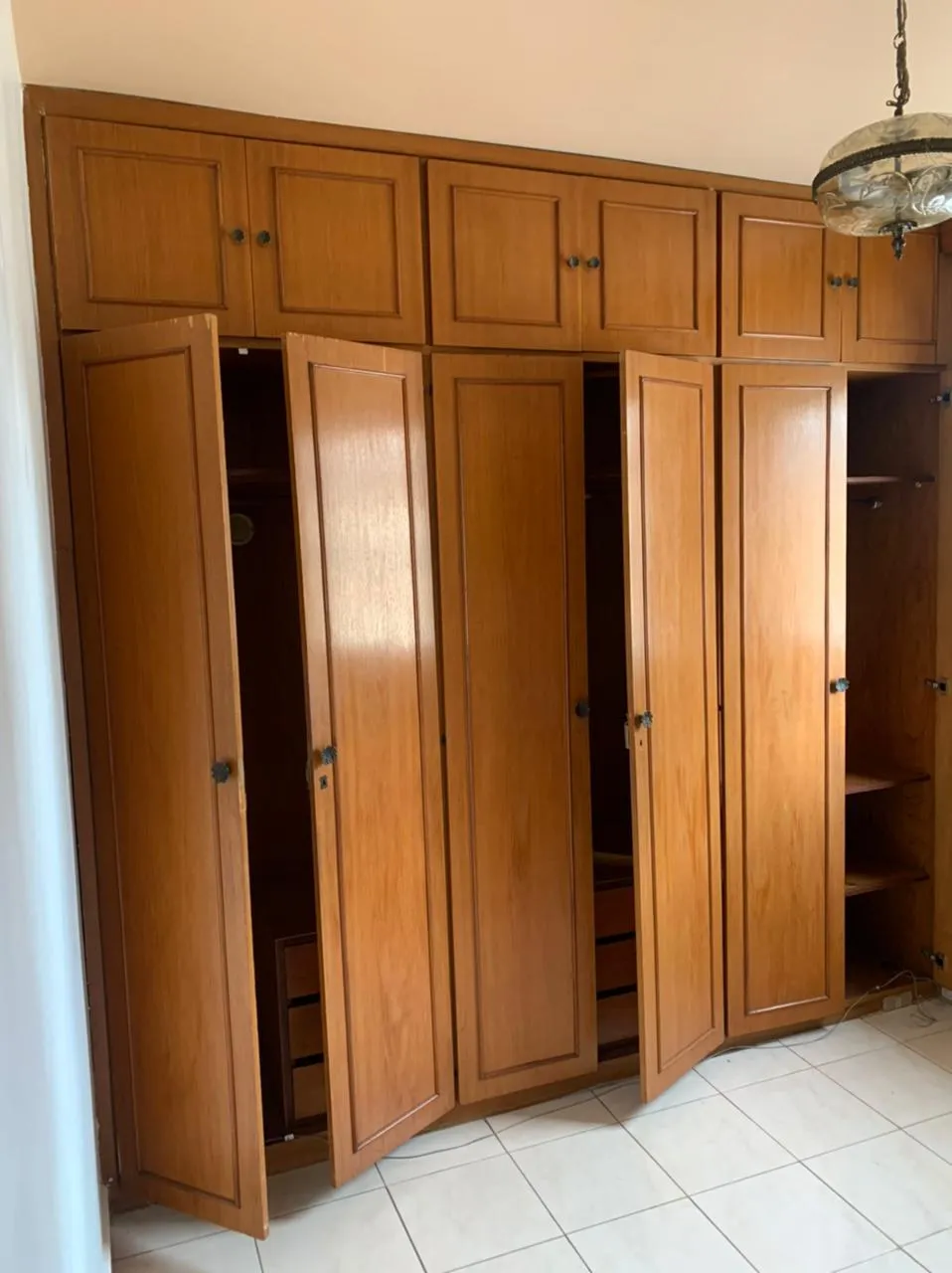 Quarto com armário embutido de madeira maciça de portas abertas e piso de cerâmica, antes da reforma