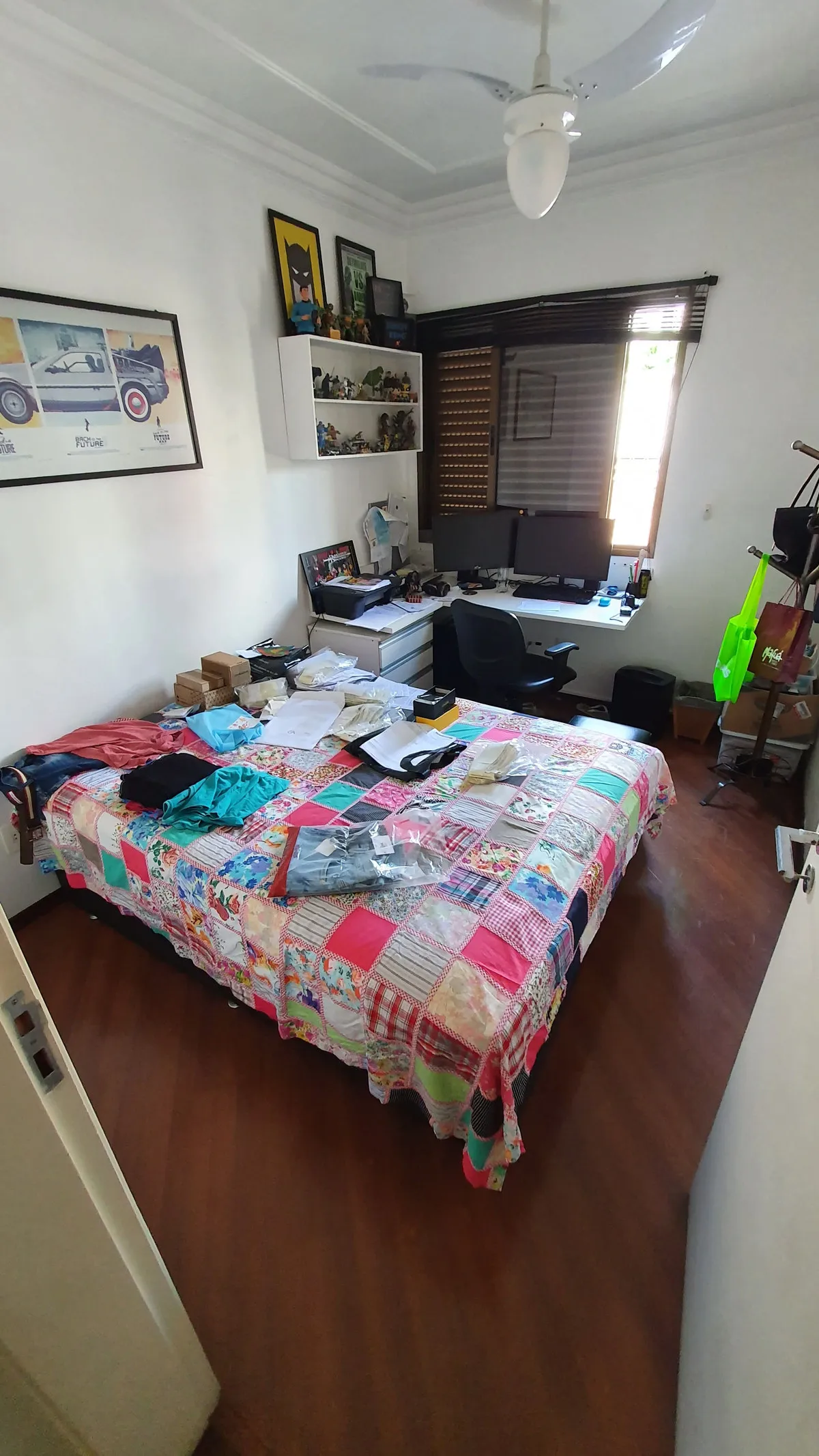 Quarto com colcha de retalhos, escrivaninha com dois monitores e pôsteres na parede, antes da reforma