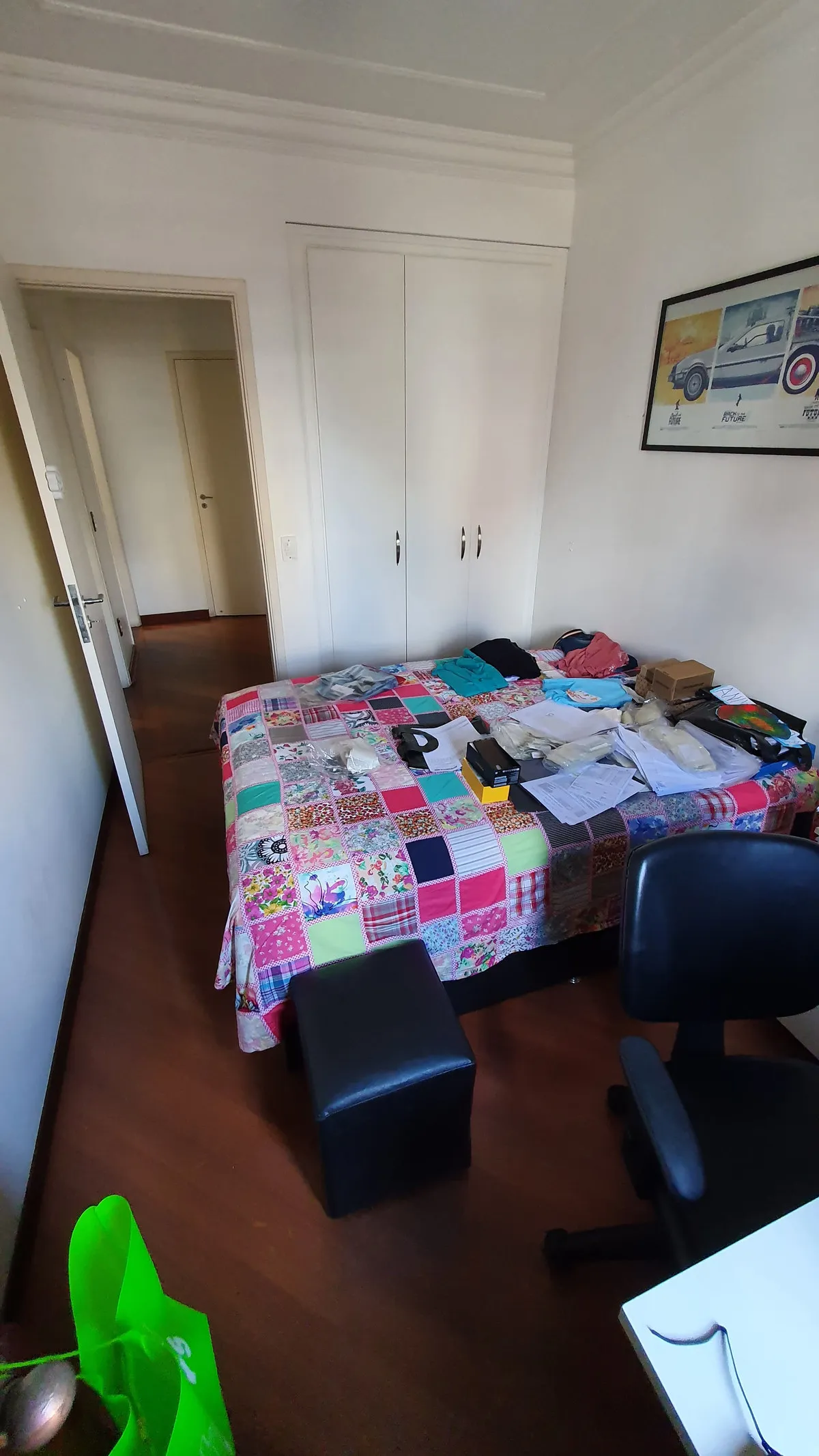Quarto com cama de colcha de retalhos, guarda-roupa branco e piso de madeira escura, antes da reforma