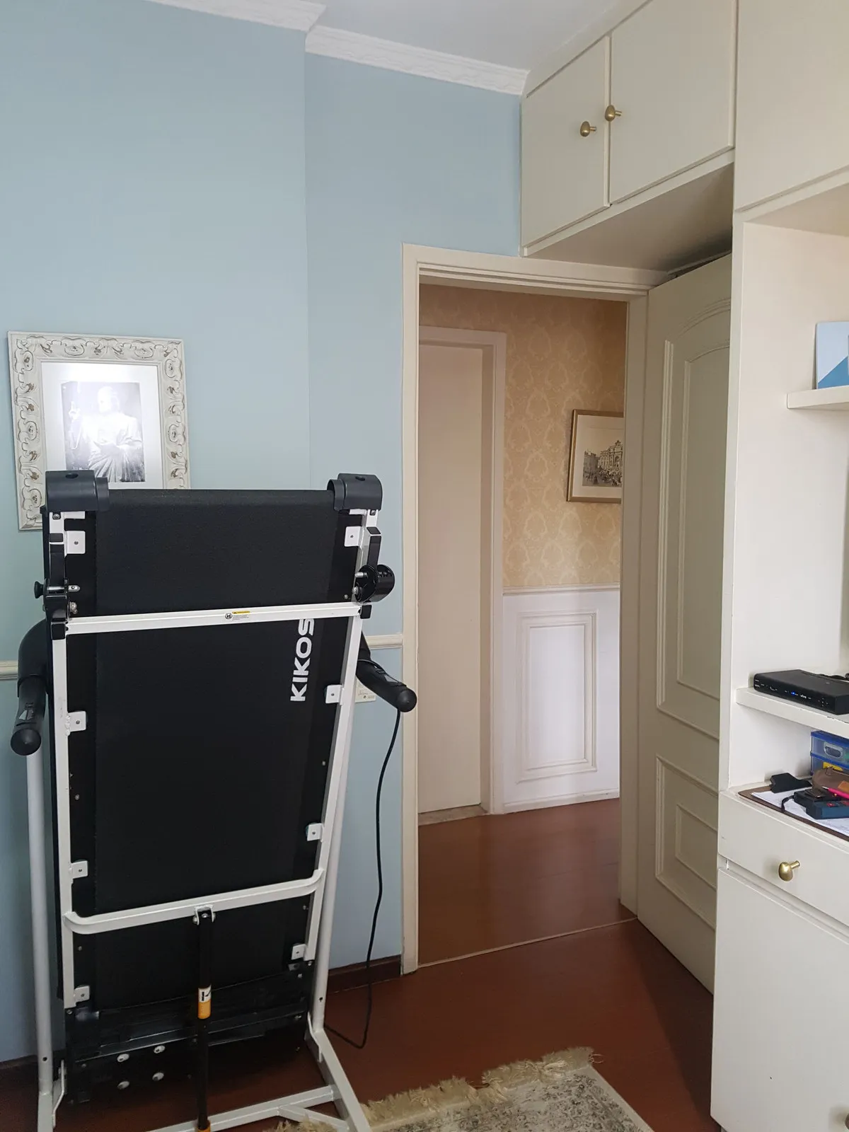 Quarto azul-claro com esteira, armários brancos embutidos e porta para o corredor, antes da reforma
