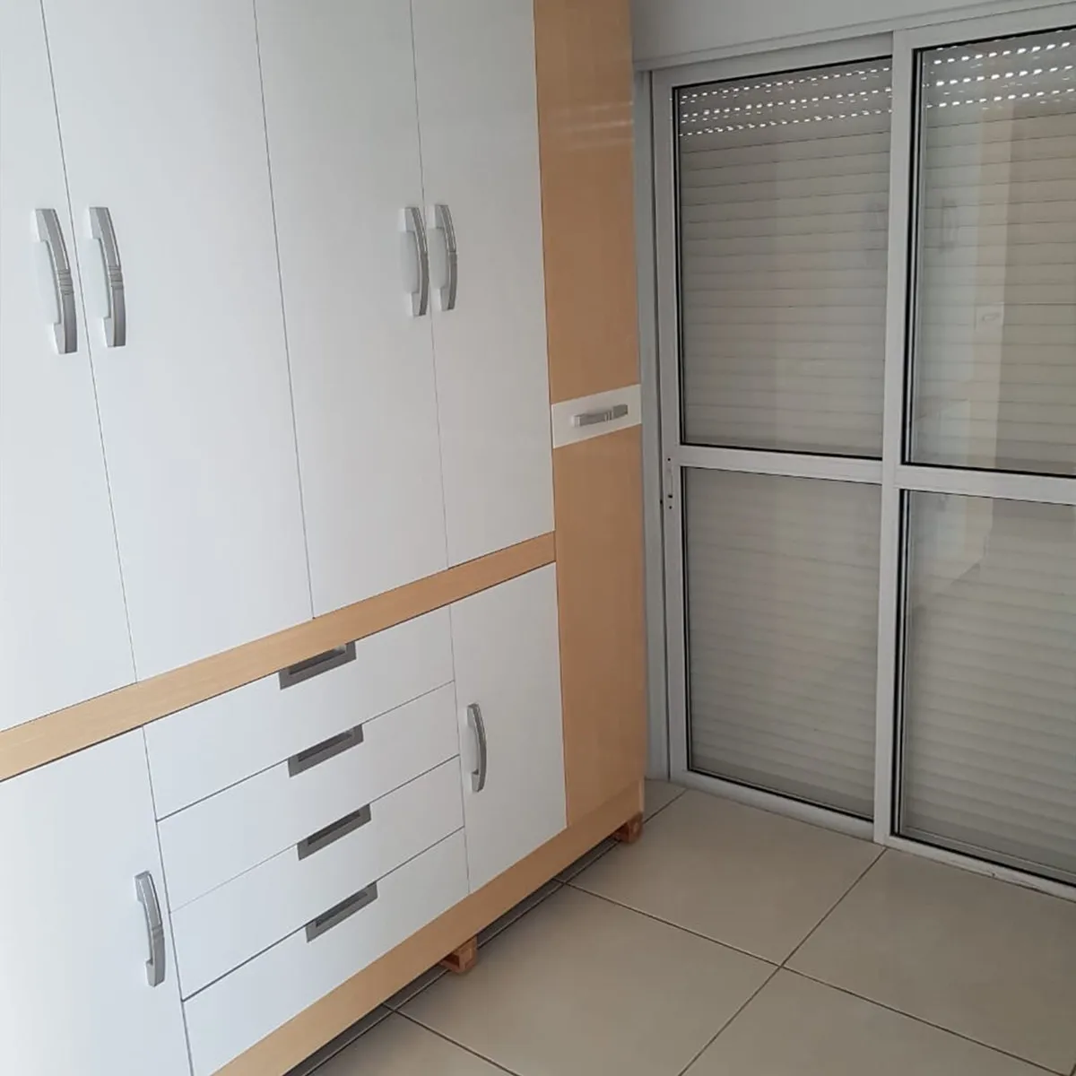 Quarto vazio com guarda-roupa branco e amadeirado e porta de correr de vidro, antes da reforma