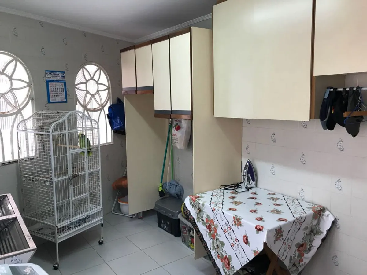 Área de serviço com armários bege, gaiola de pássaro, tábua de passar e janelas arqueadas vazadas, antes da reforma