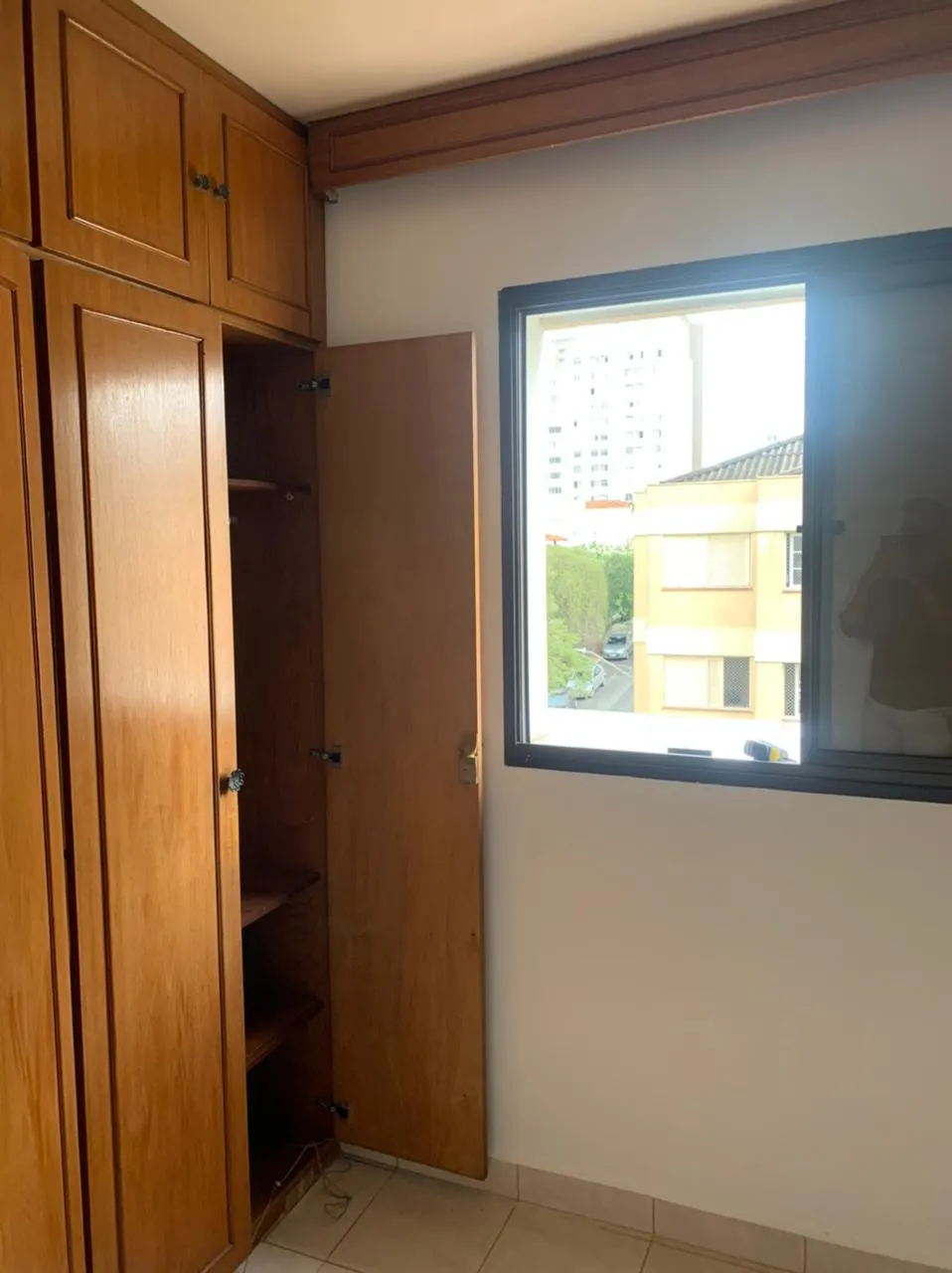 Quarto com armário embutido de madeira de portas abertas e janela com vista da cidade, antes da reforma