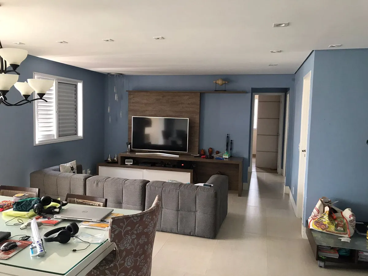Sala de estar com paredes azuis, sofá cinza e painel de madeira com TV, antes da reforma