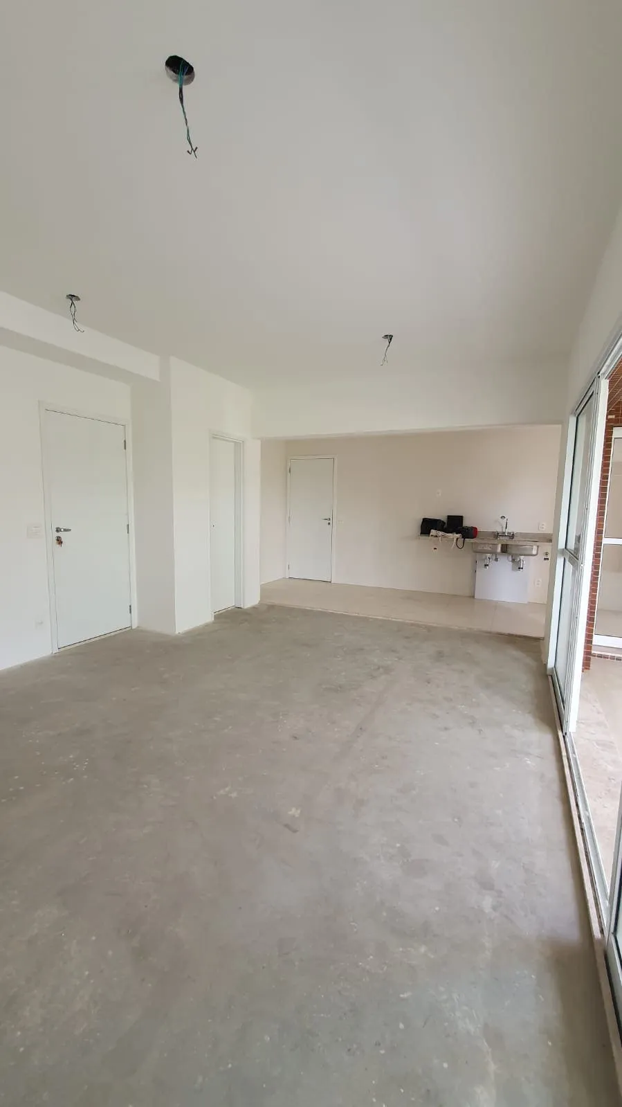 Living vazio com contrapiso cinza, portas brancas e ponto de pia provisório junto à varanda, antes da reforma