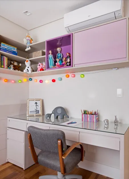 Bancada de estudo branca com cadeira cinza, nichos com bonecas e pelúcias, cordão de luzes e armário rosa, antes da reforma