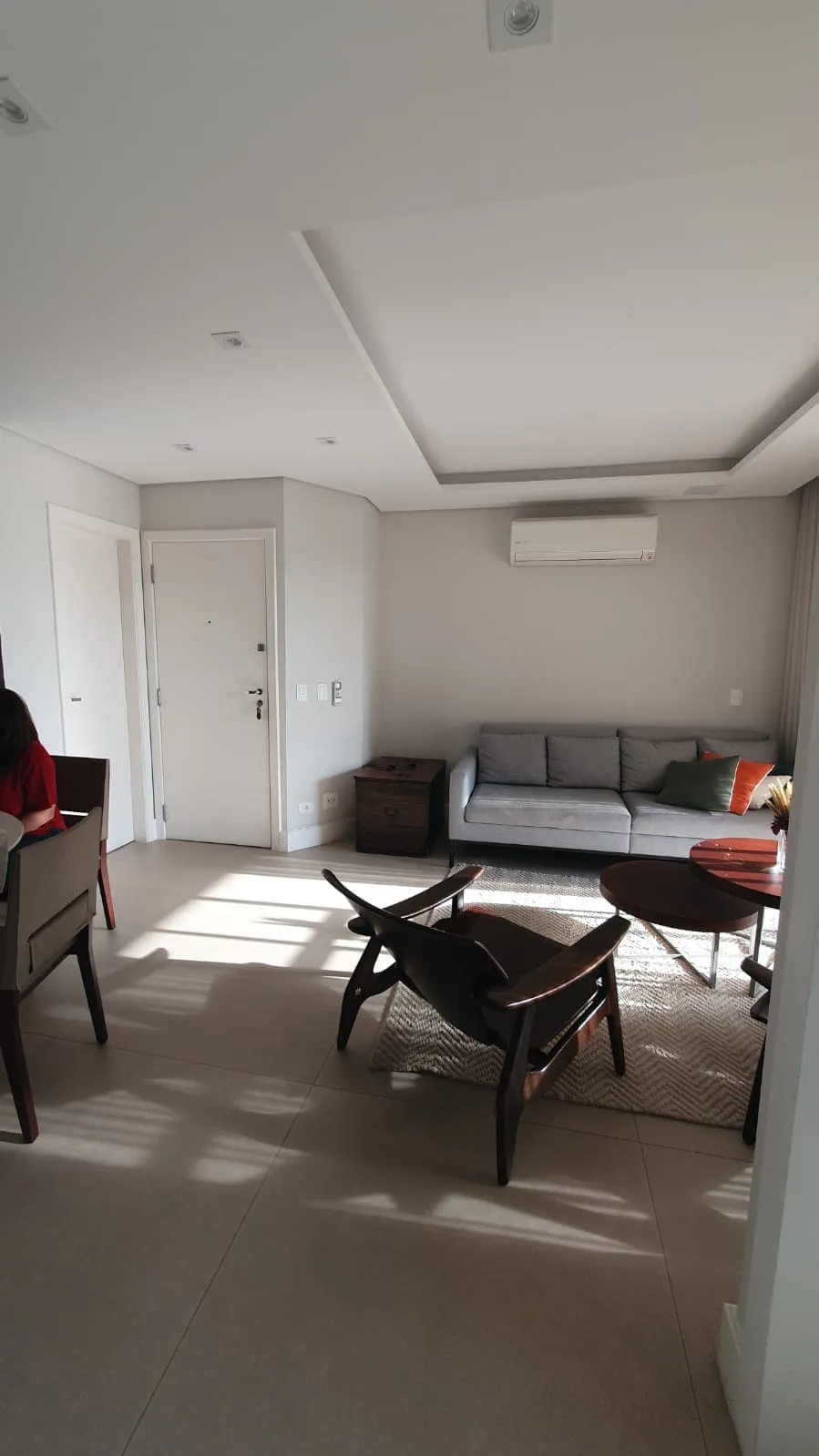 Sala antiga com sofá cinza, poltronas de madeira escura e tapete de juta, antes da reforma