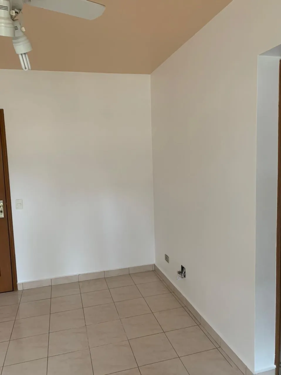 Quarto vazio com ventilador de teto, teto pintado de bege, paredes brancas e piso de cerâmica, antes da reforma