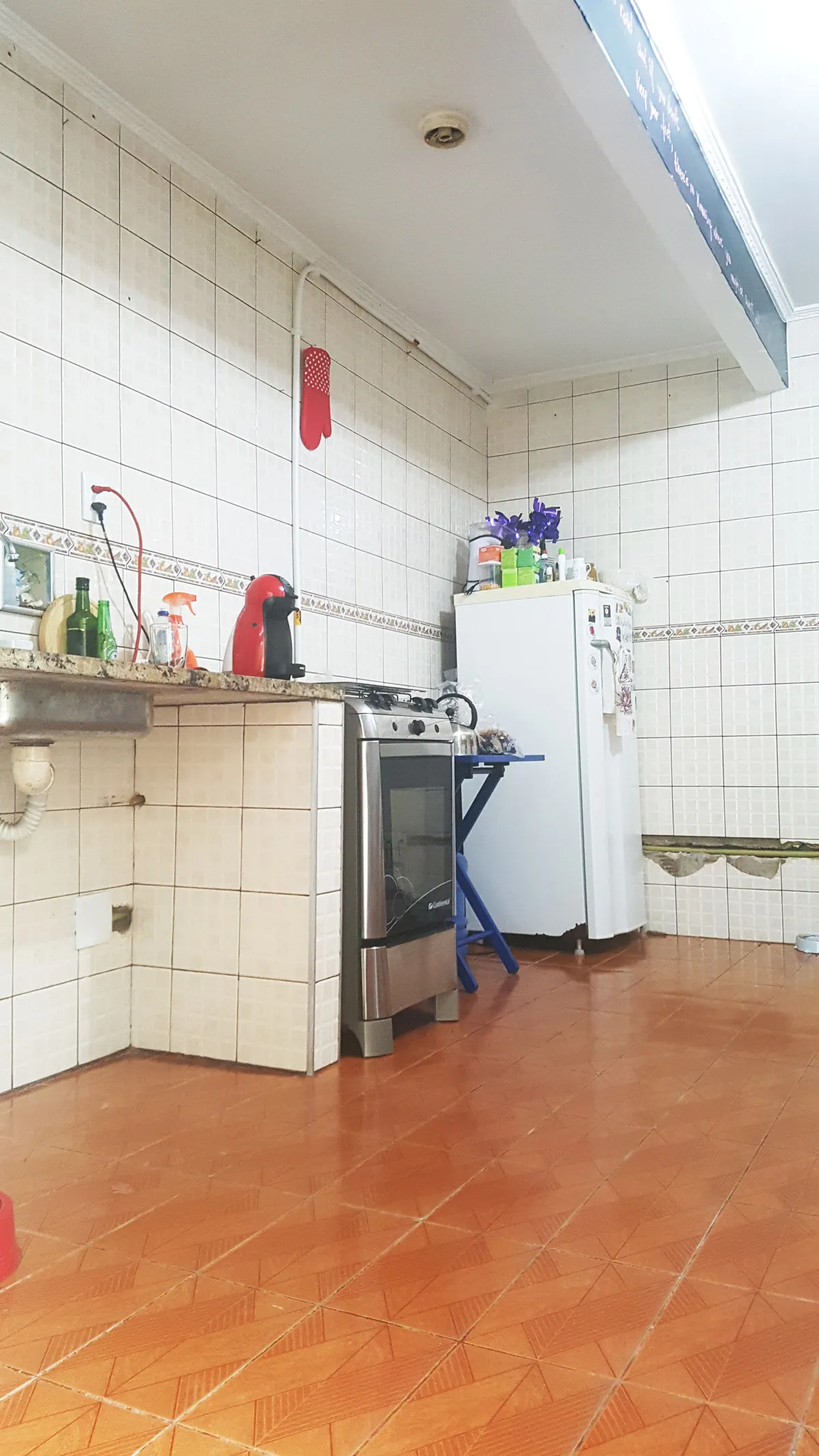 Cozinha antiga com azulejo branco, bancada de granito, fogão de inox e geladeira coberta de imãs, antes da reforma