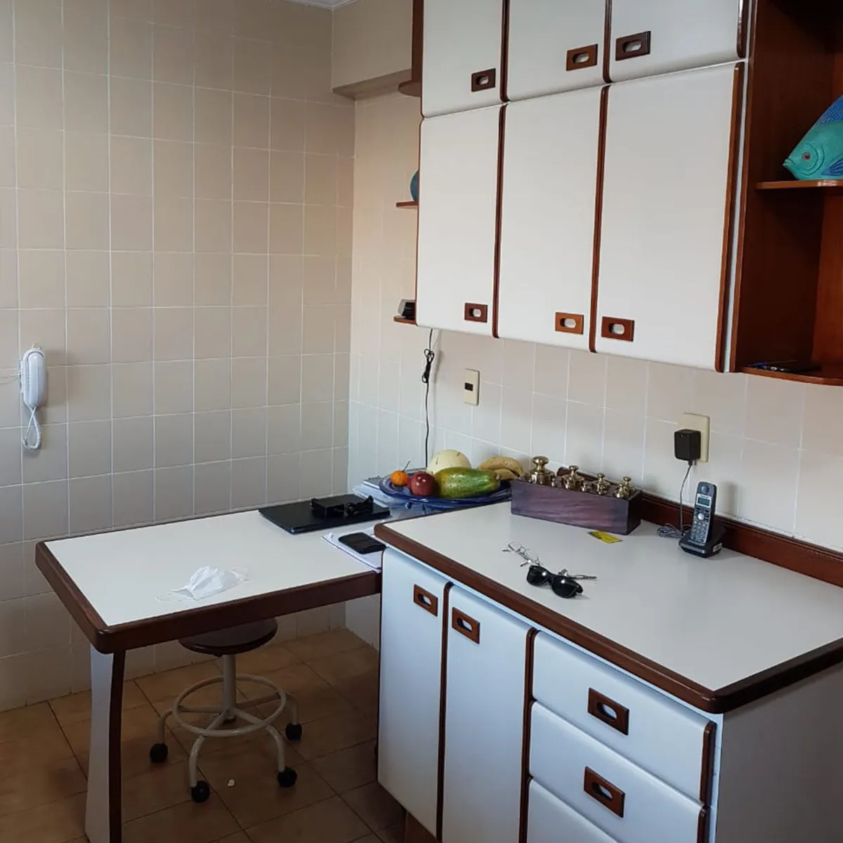 Copa antiga com parede de azulejo branco, armários de laminado com friso marrom e mesa dobrável, antes da reforma