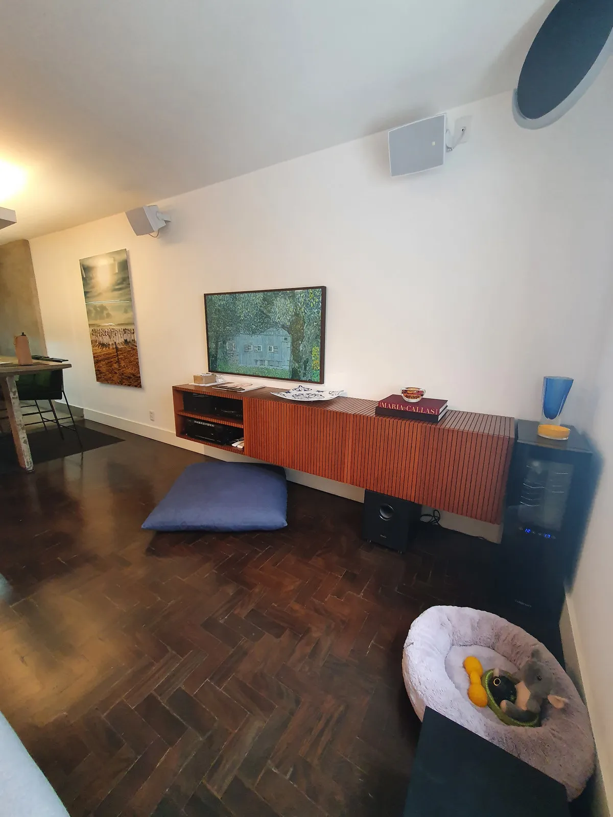 Parede branca com rack ripado laranja e TV, piso de taco escuro em espinha de peixe, antes da reforma