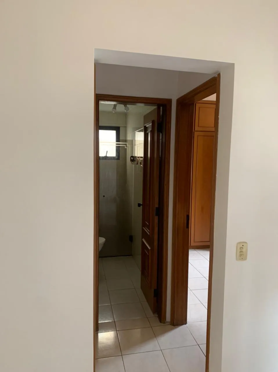 Corredor com portas de madeira dando para o banheiro e um quarto, piso de cerâmica, antes da reforma