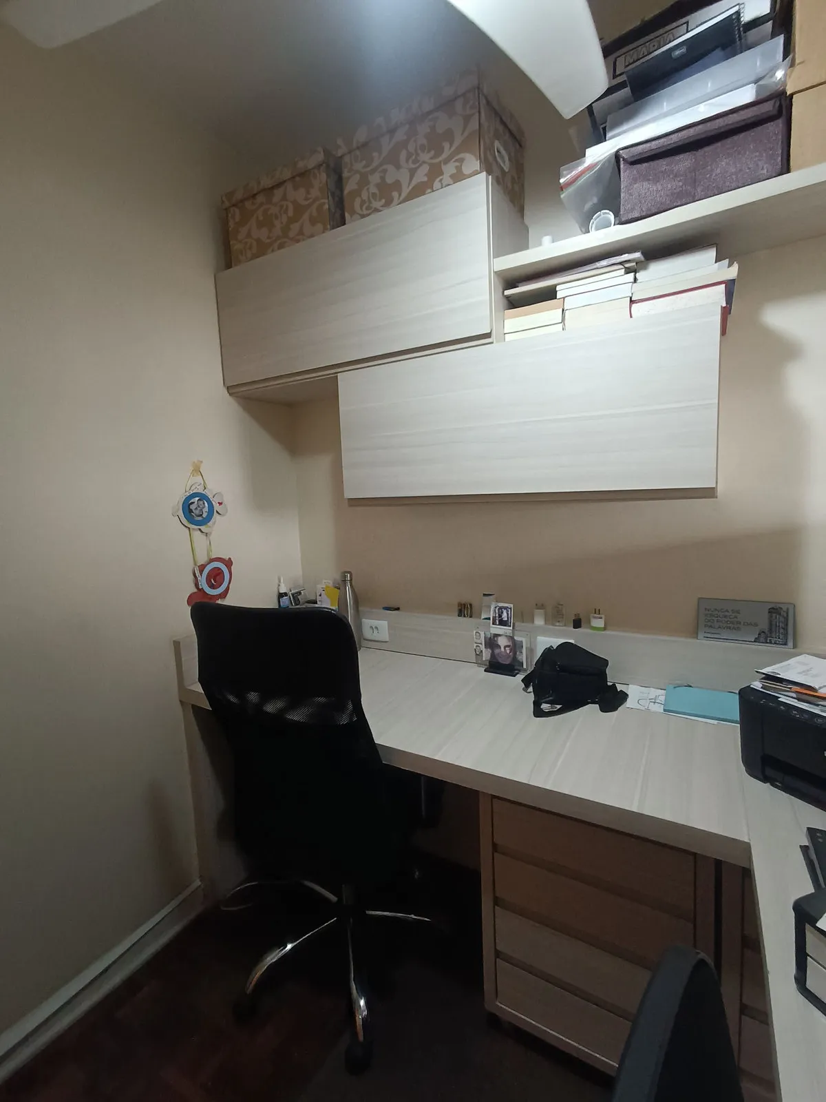 Home office compacto com bancada clara, armários suspensos, cadeira preta e piso escuro, antes da reforma