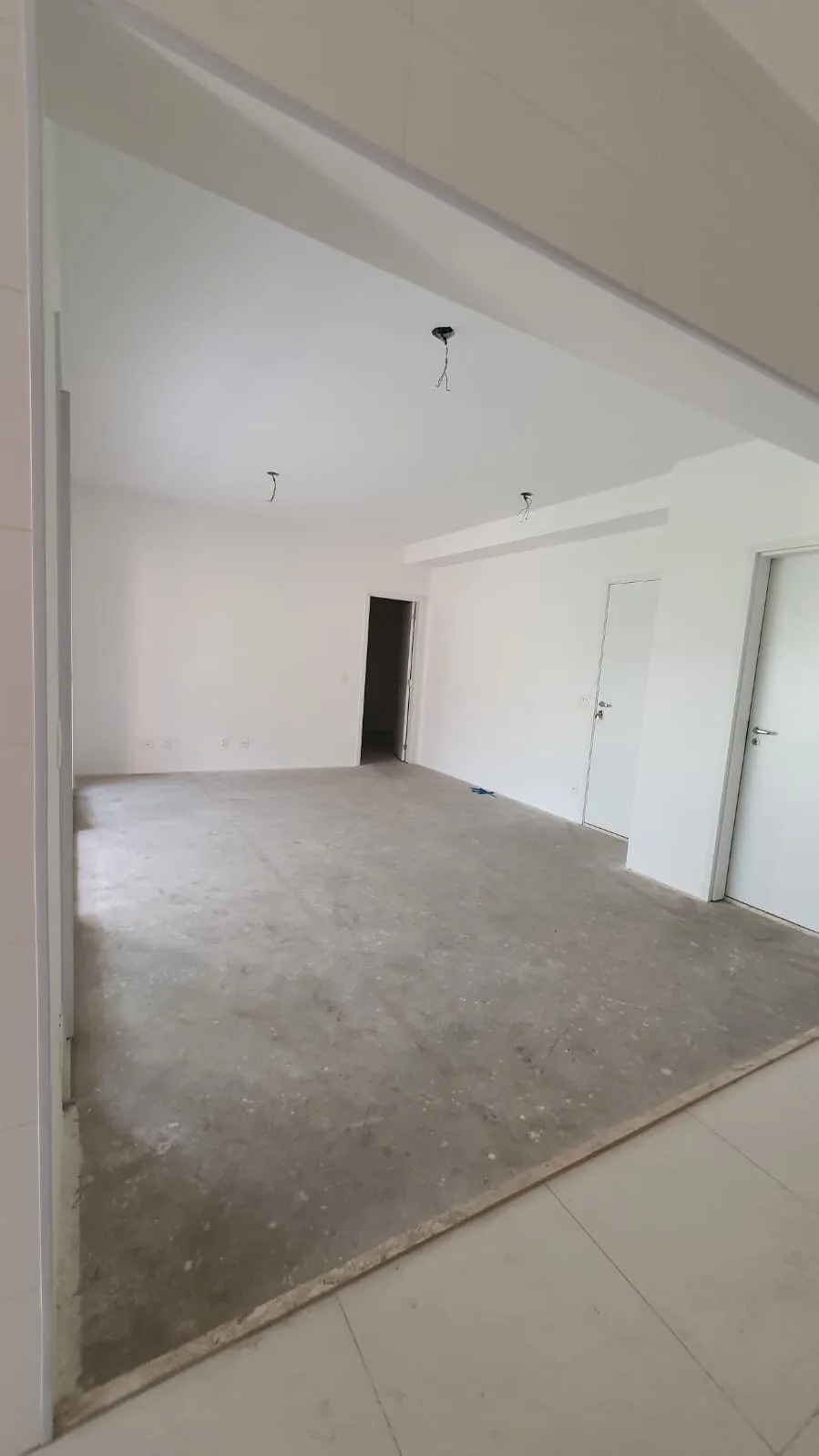 Ambiente vazio visto da varanda, contrapiso sem revestimento, paredes brancas e portas de acesso aos quartos, antes da reforma