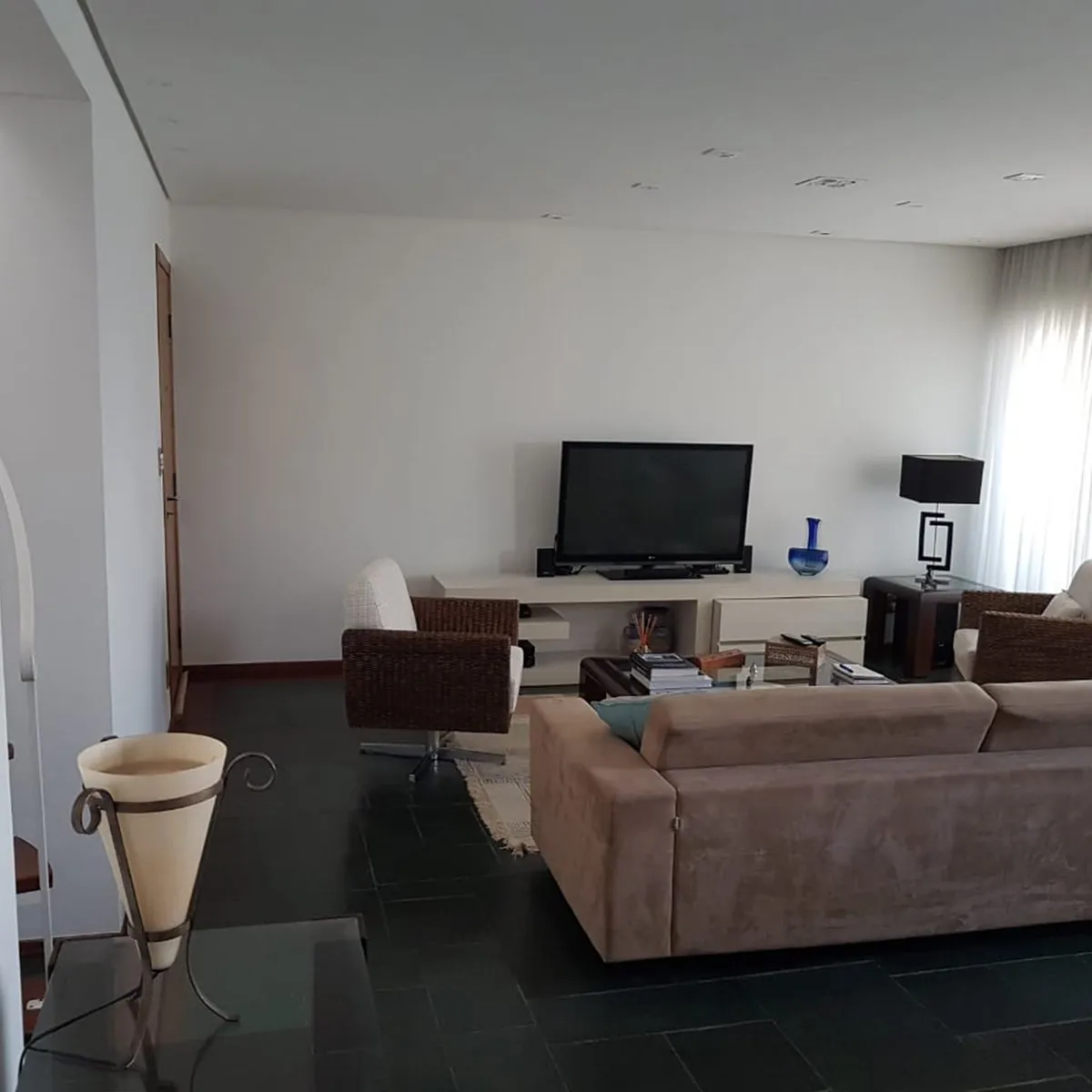 Living com TV sobre rack branco, poltronas de vime e piso de ardósia escura, antes da reforma