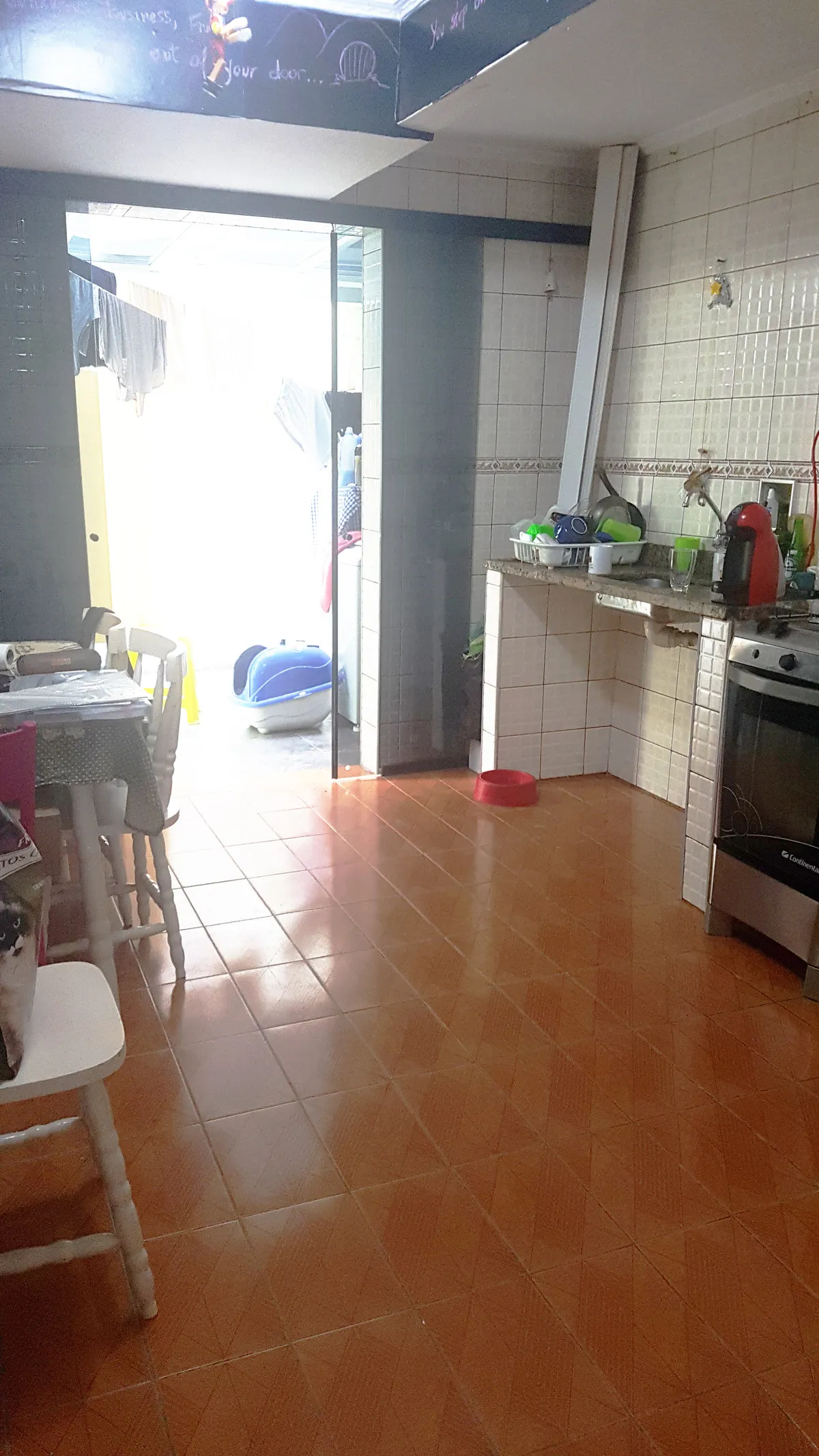Cozinha com piso vermelho e azulejo branco aberta para a área de serviço iluminada, antes da reforma