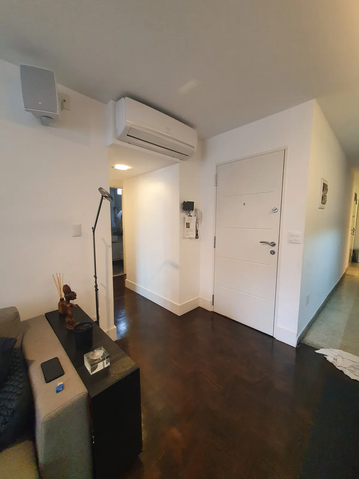 Hall de entrada com porta branca, ar-condicionado split e piso de taco escuro, antes da reforma