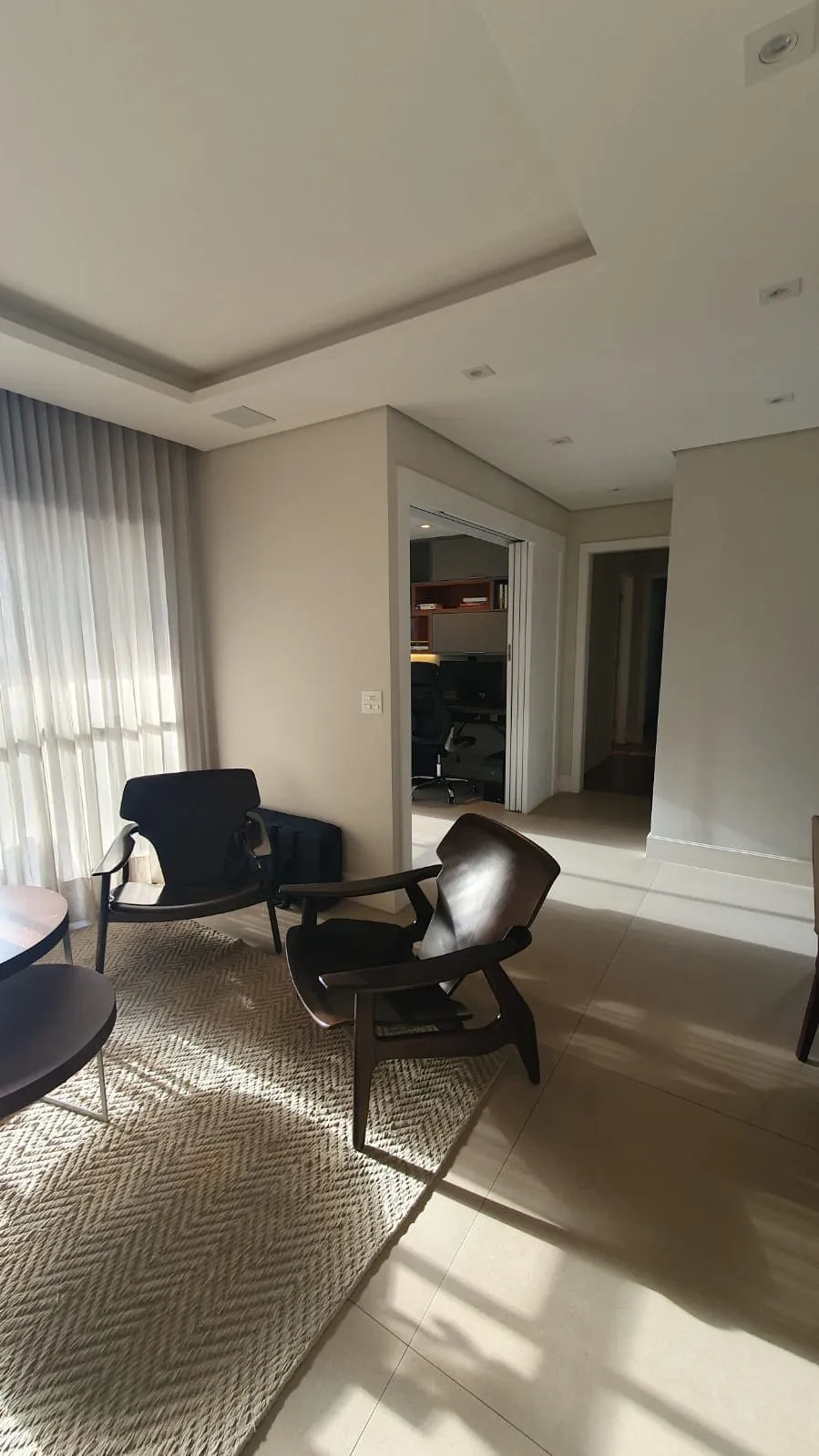 Estar antigo com poltronas de madeira, cortina de voile e escritório visível pela porta de correr, antes da reforma