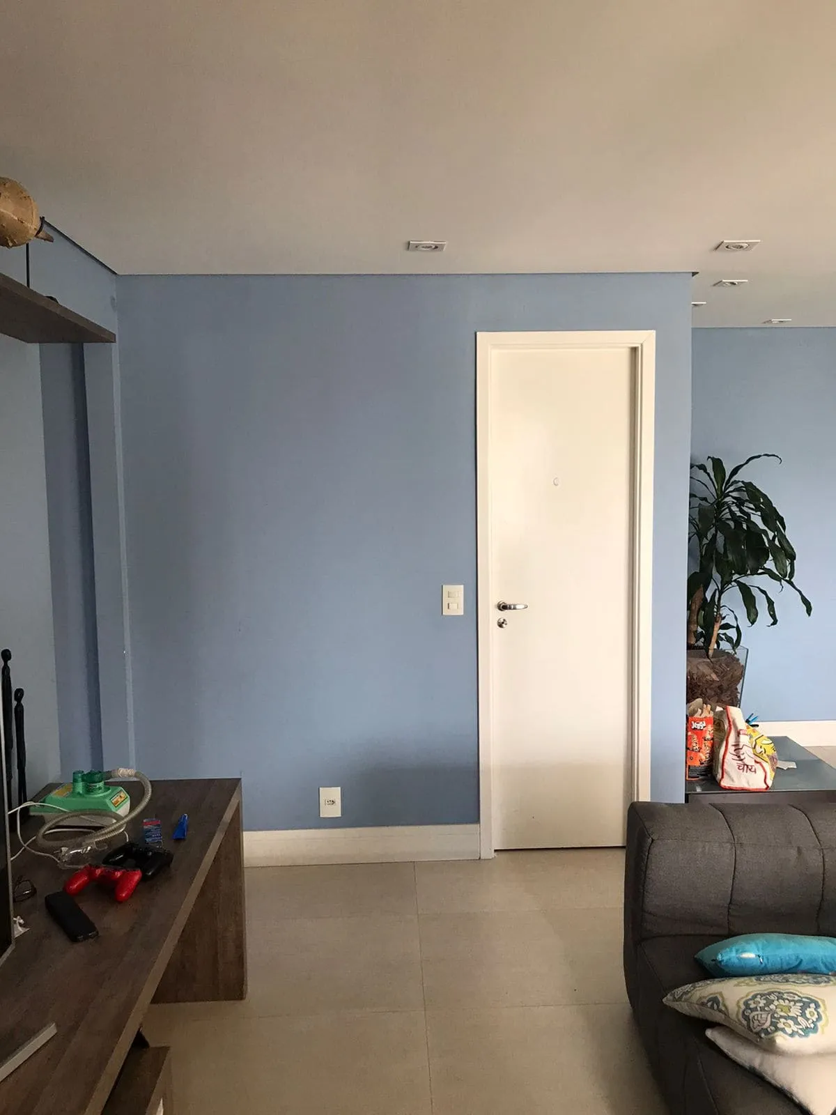 Sala com paredes azuis, porta branca, aparador de madeira e sofá cinza, antes da reforma