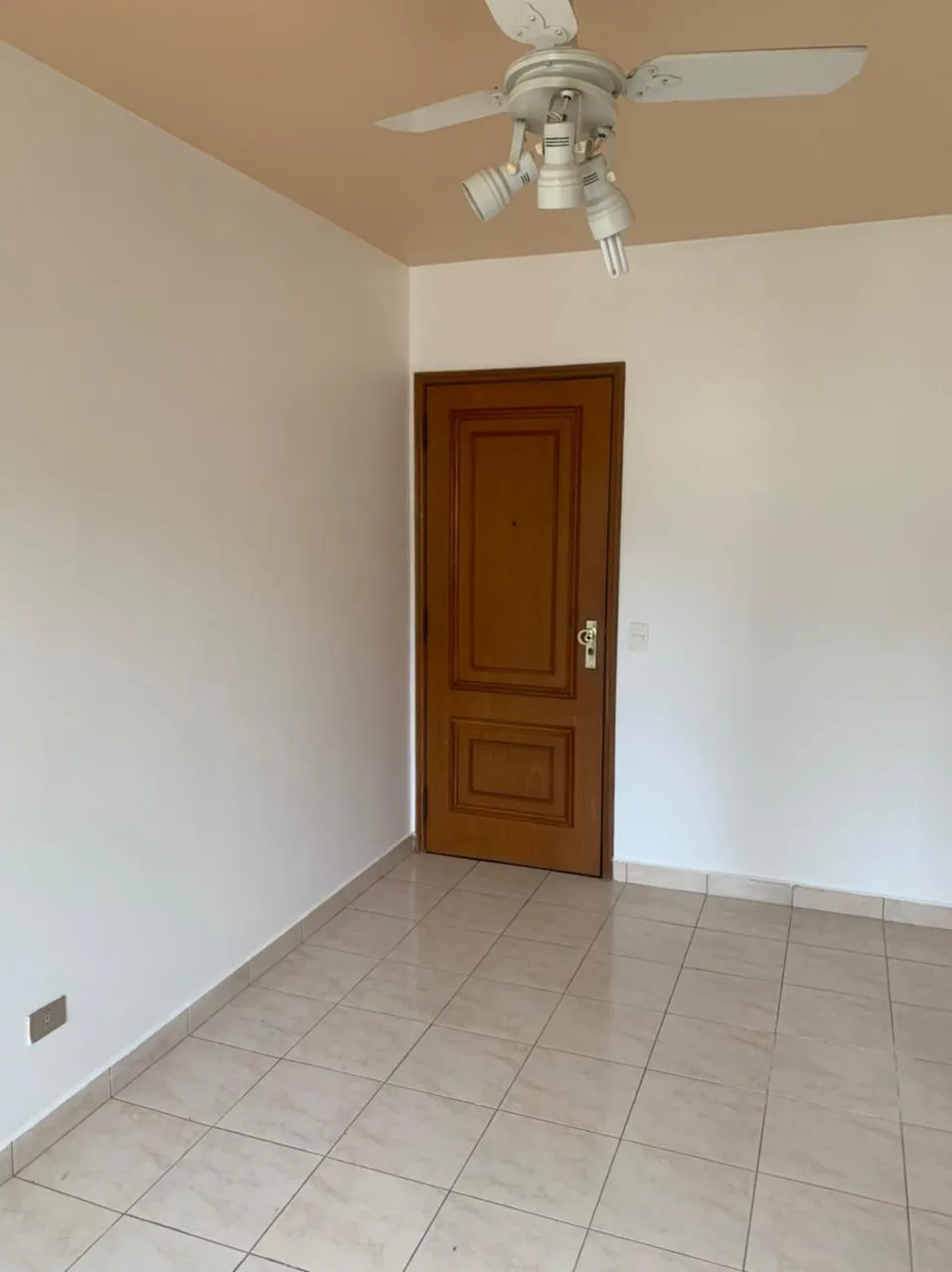 Cômodo vazio com ventilador de teto com spots, porta de madeira envernizada e piso de cerâmica, antes da reforma